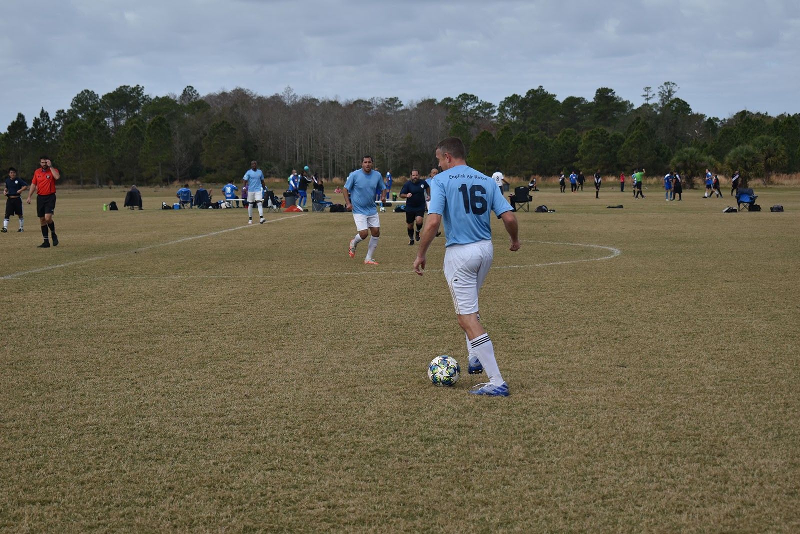 Soccer player in light blue jersey dribbles on a grassy field during a match