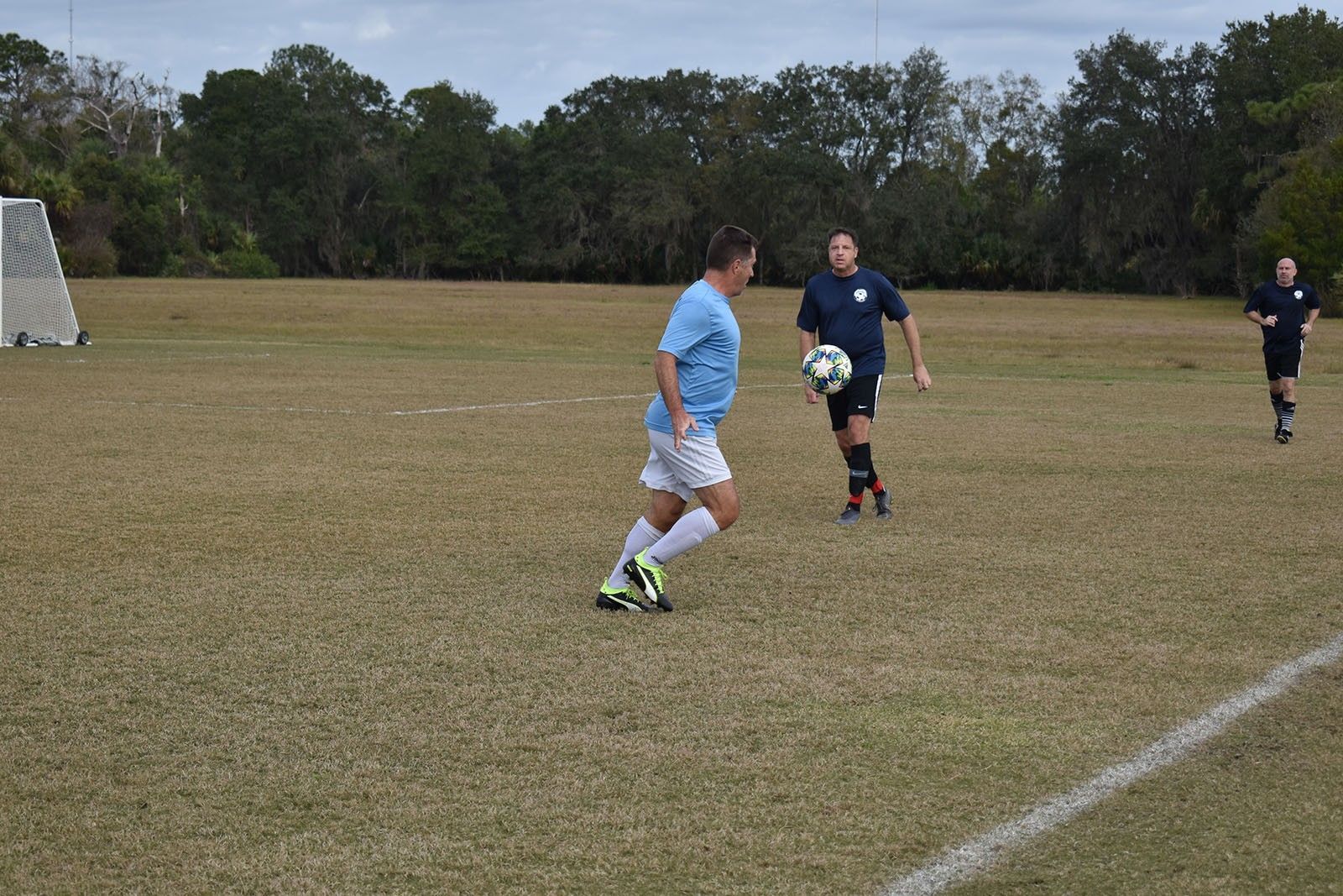 Soccer players in blue uniforms compete on a grassy field near a goal.