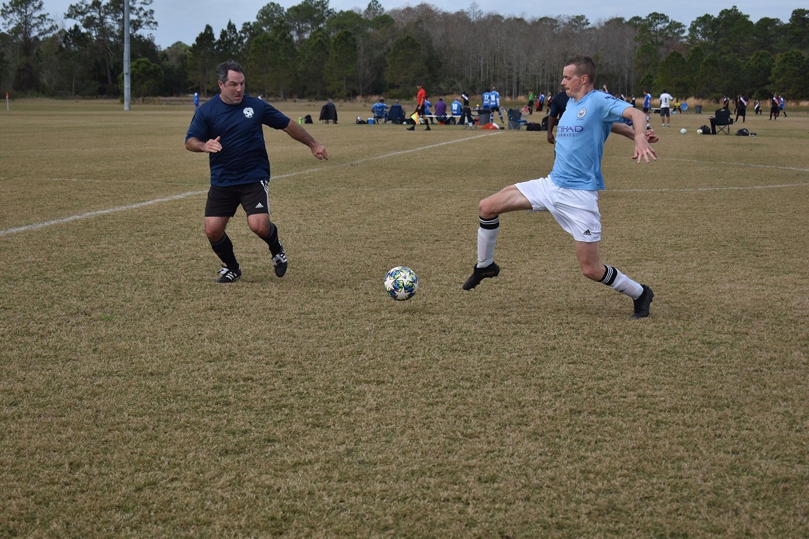 Two soccer players in blue jerseys contest the ball on a grassy field.