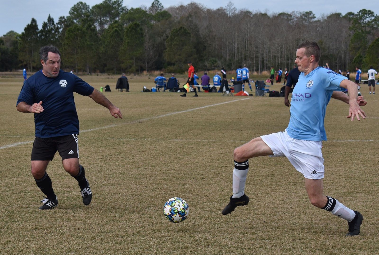 Two soccer players in blue uniforms contest the ball on a grassy field.