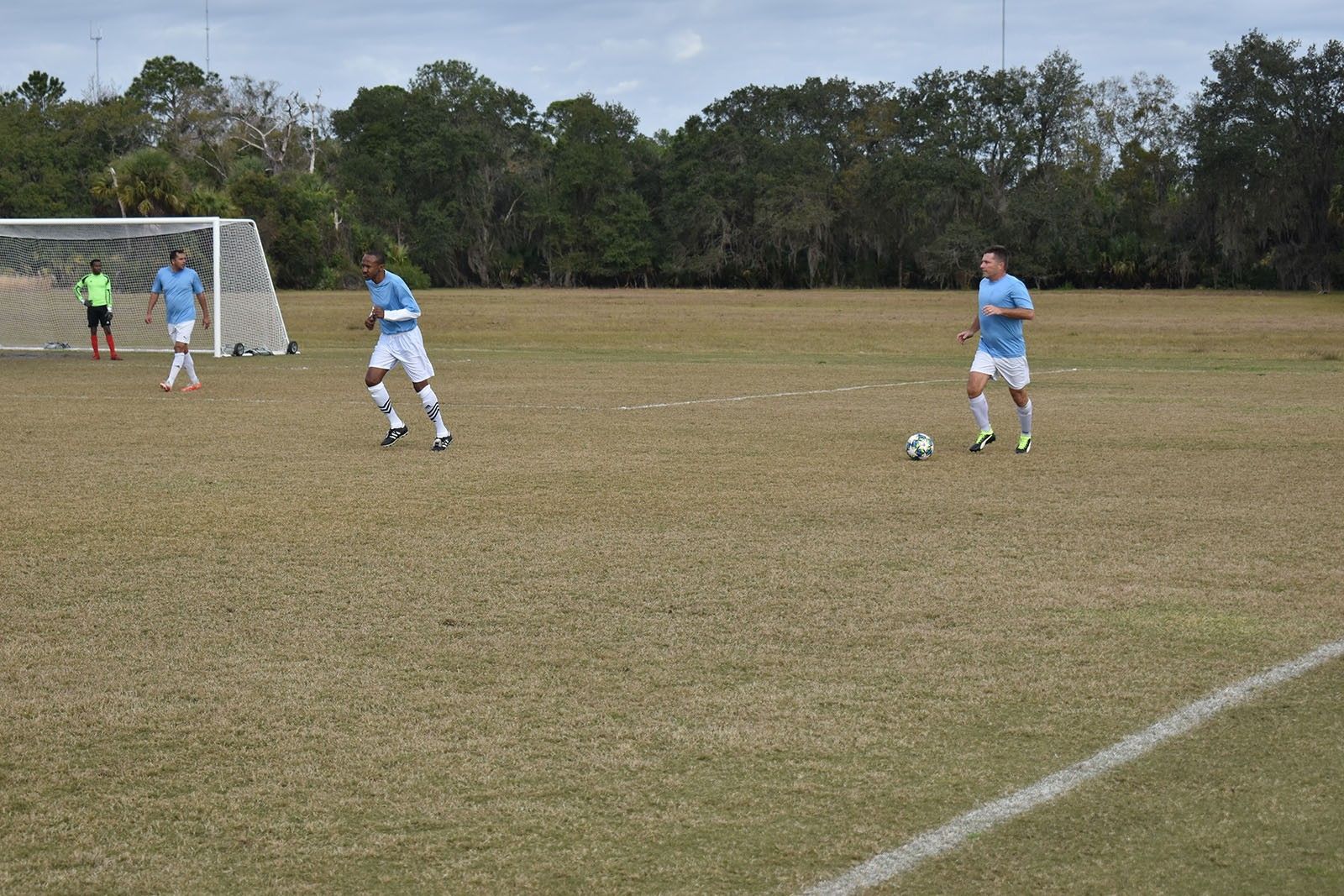 Soccer players on a grassy field near the goal, with one player preparing to kick the ball.