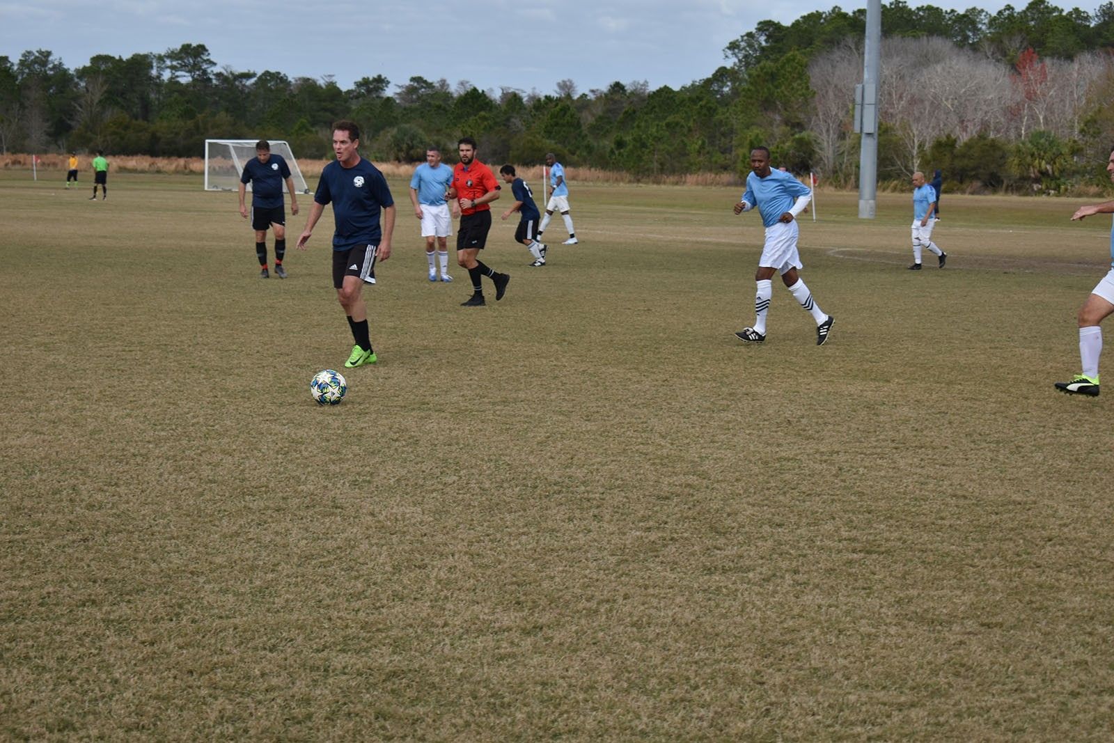Youth soccer players practice on a grassy field, with one player dribbling a ball in the foreground.