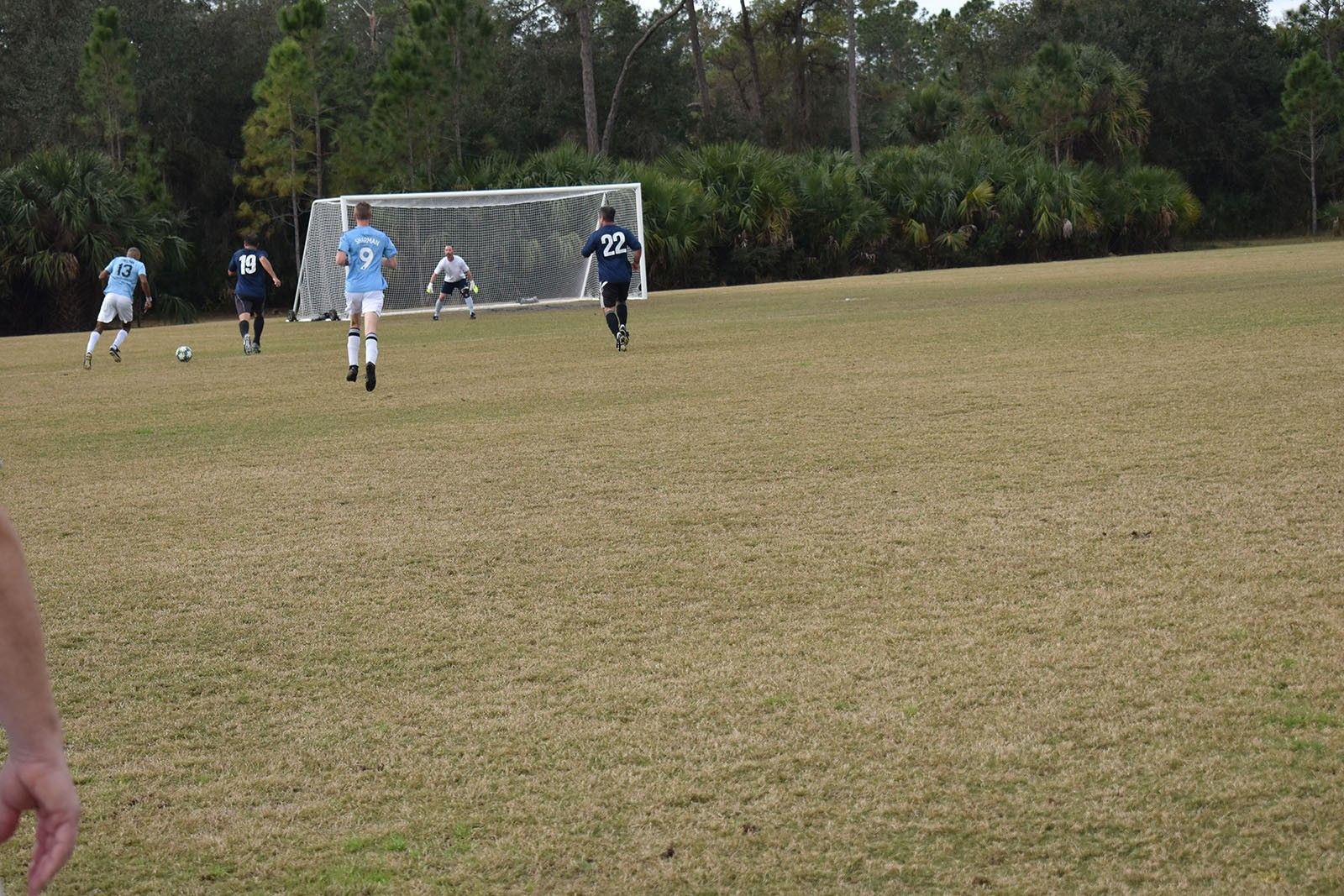 Youth soccer game near goal on a grassy field, with players in blue and white uniforms.