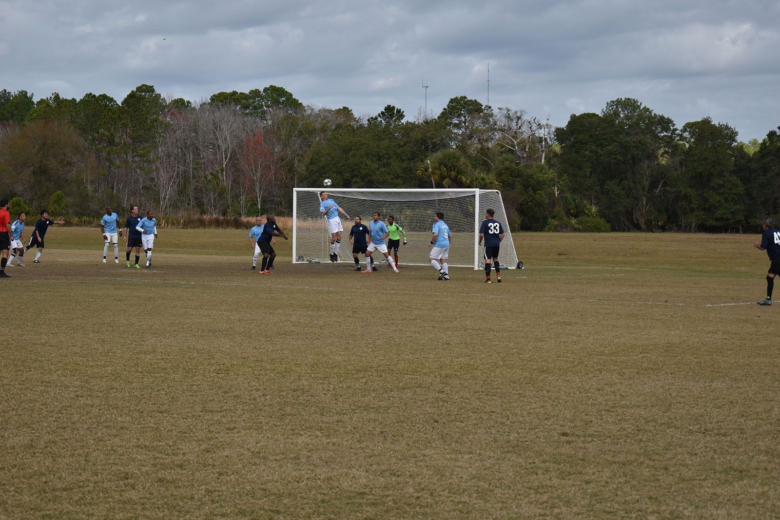 Youth soccer players around a goal on a grassy field under cloudy skies