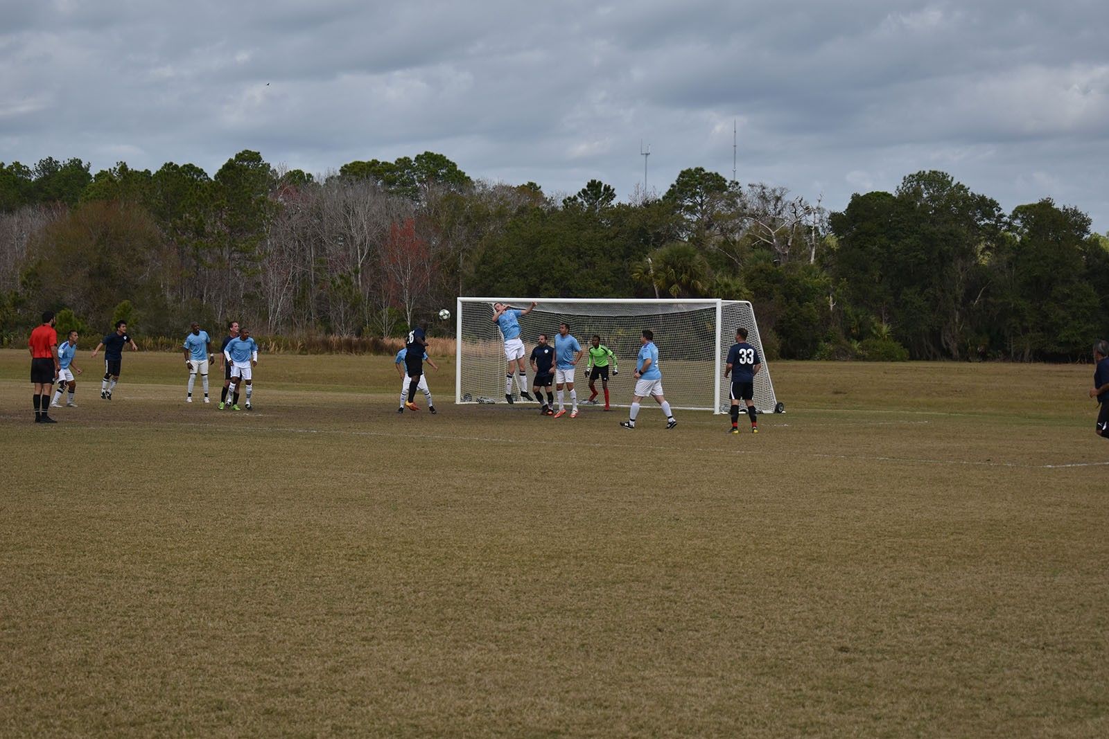 Soccer match on a grassy field, players gathered near the goal under an overcast sky.