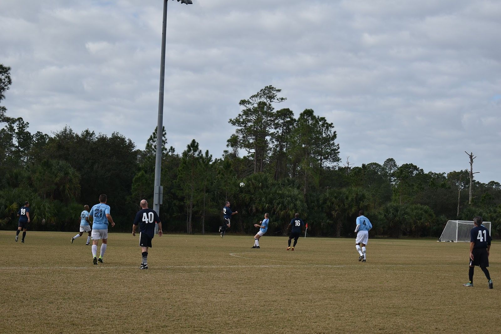 Soccer players in blue and black uniforms on a grassy field under a cloudy sky.