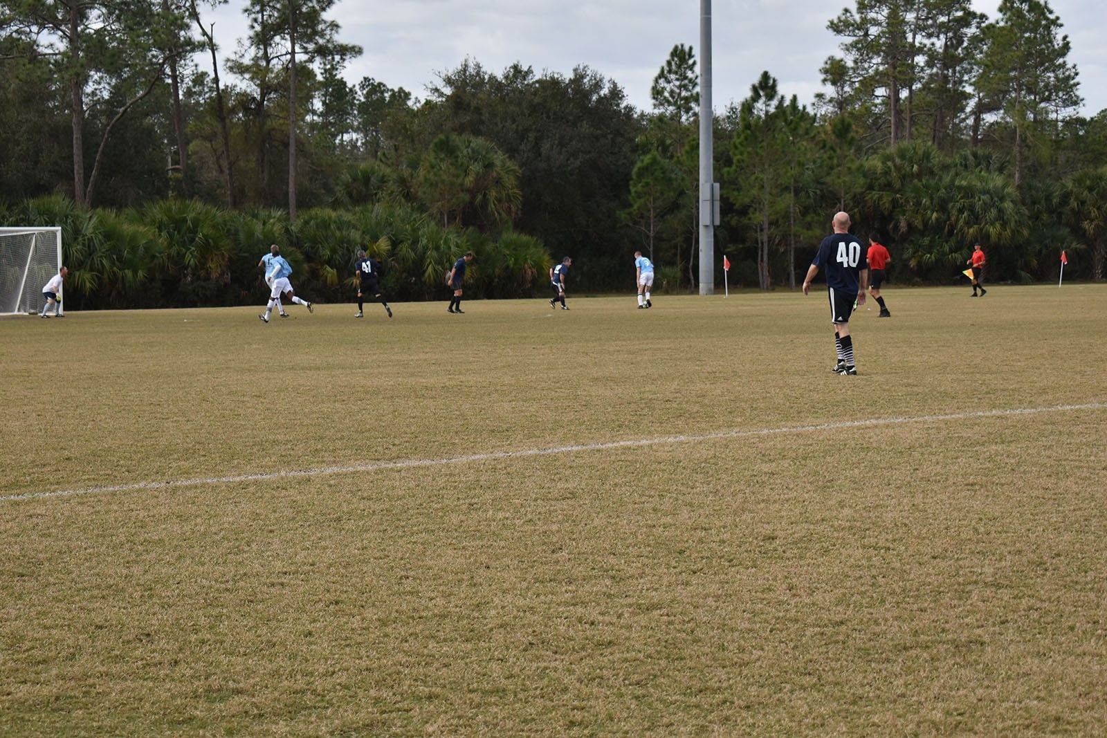 Soccer players on a grassy field near a goal, with one player in a black jersey in the foreground.