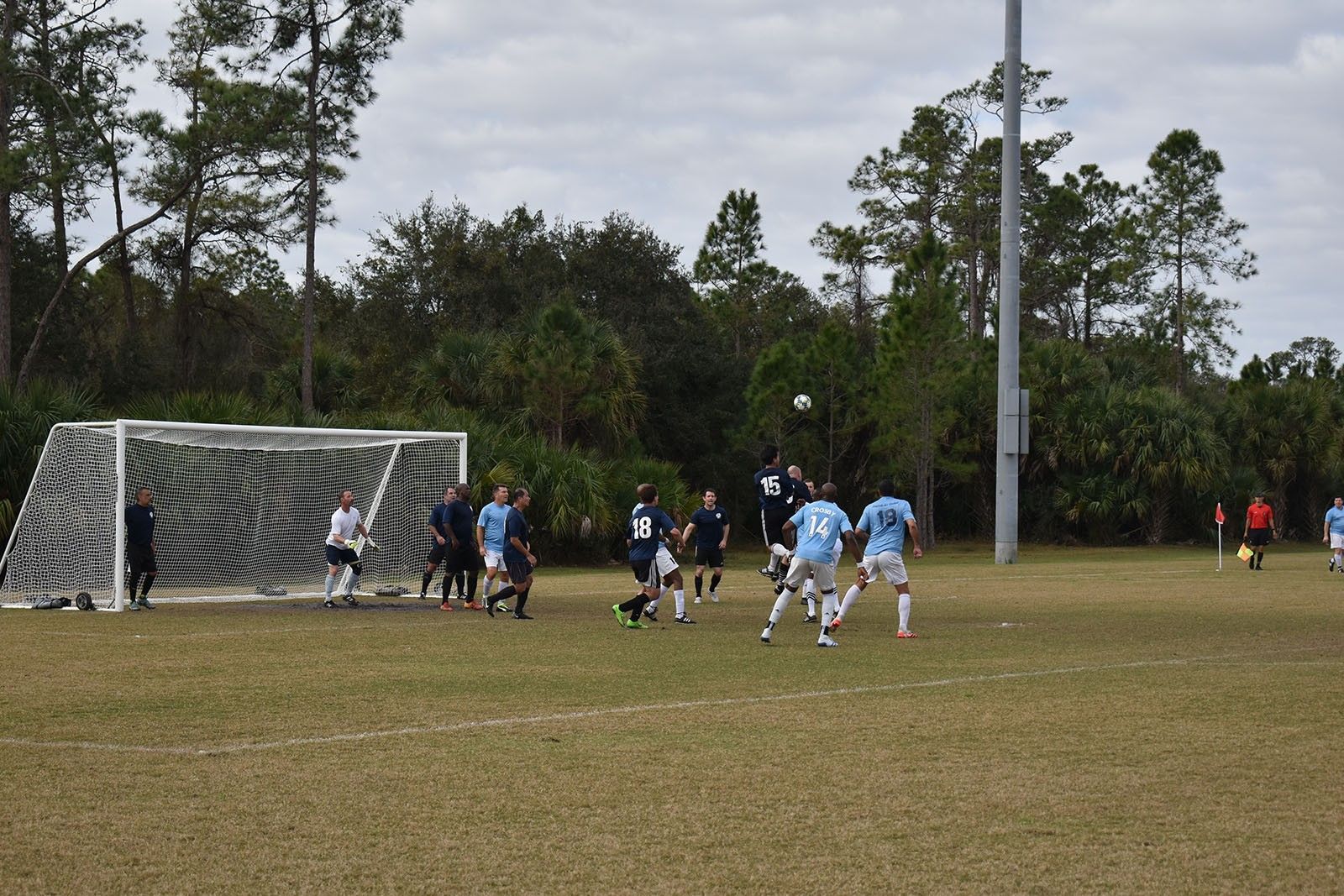 Soccer game near the goal, with players in blue and black contesting the ball on a grassy field.