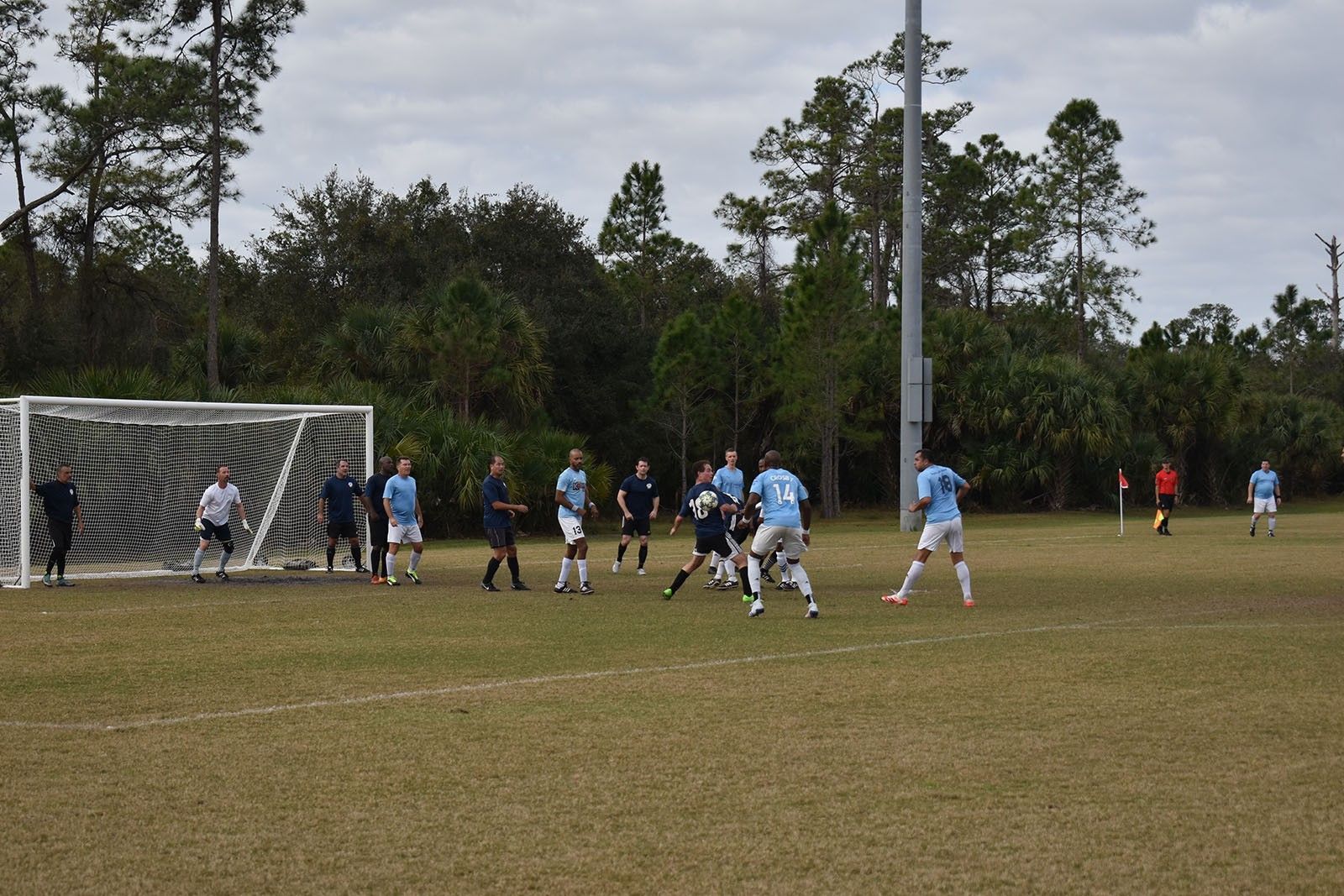 Soccer match near the goal on a grassy field, with players in light blue and white uniforms.