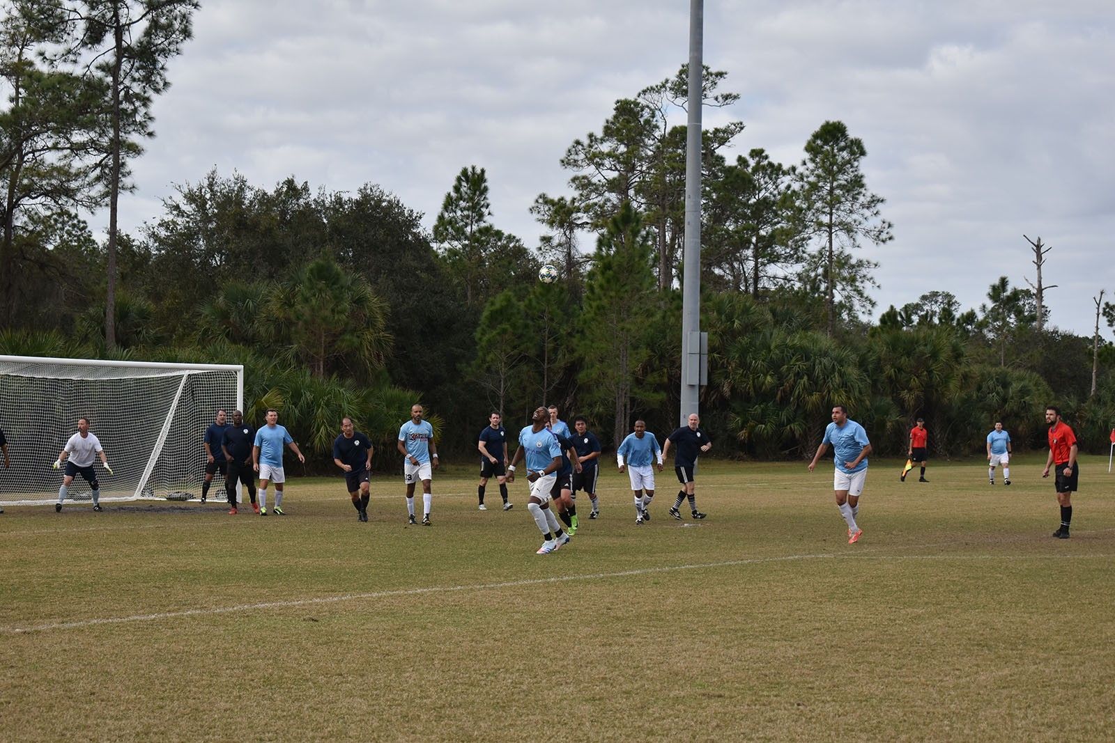 Soccer players in blue and black uniforms compete near the goal on a grassy field.