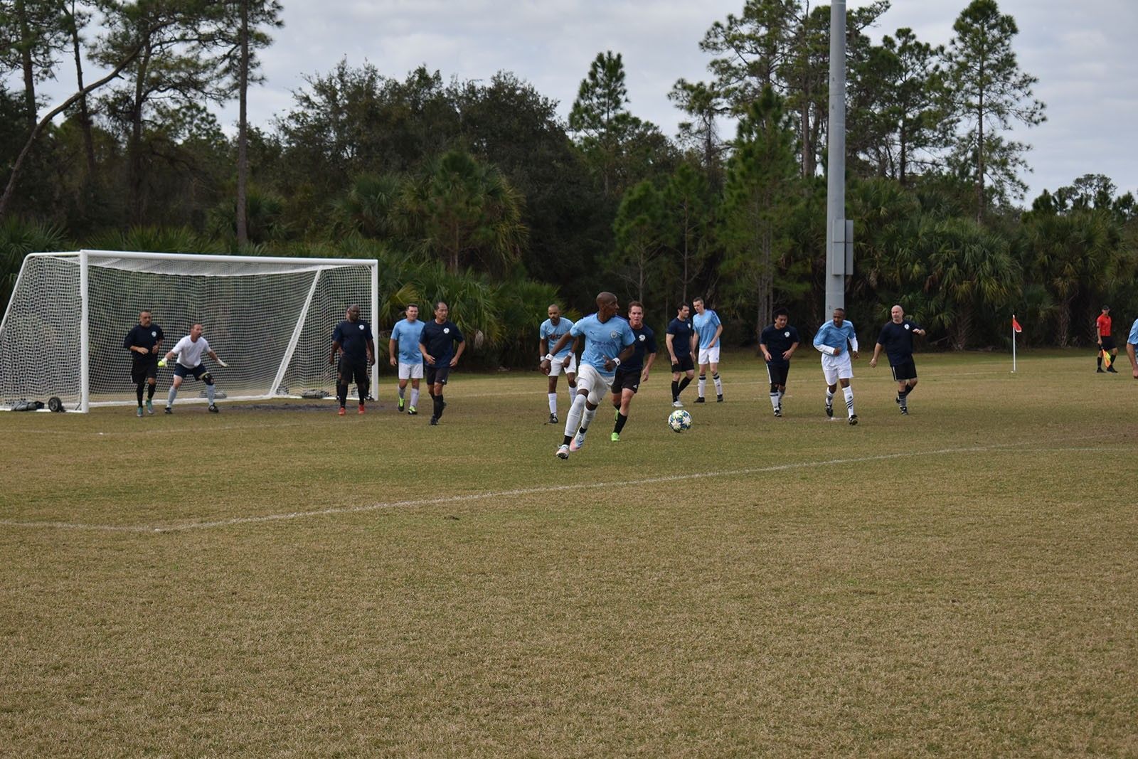 Soccer match near the goal on a grassy field, with players in blue and black chasing the ball.