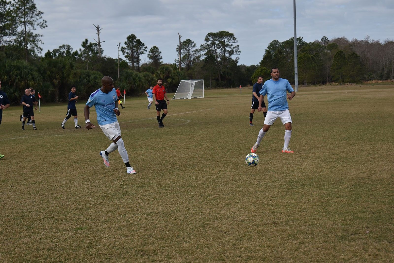 Two soccer players in blue uniforms compete for the ball on a grassy field.