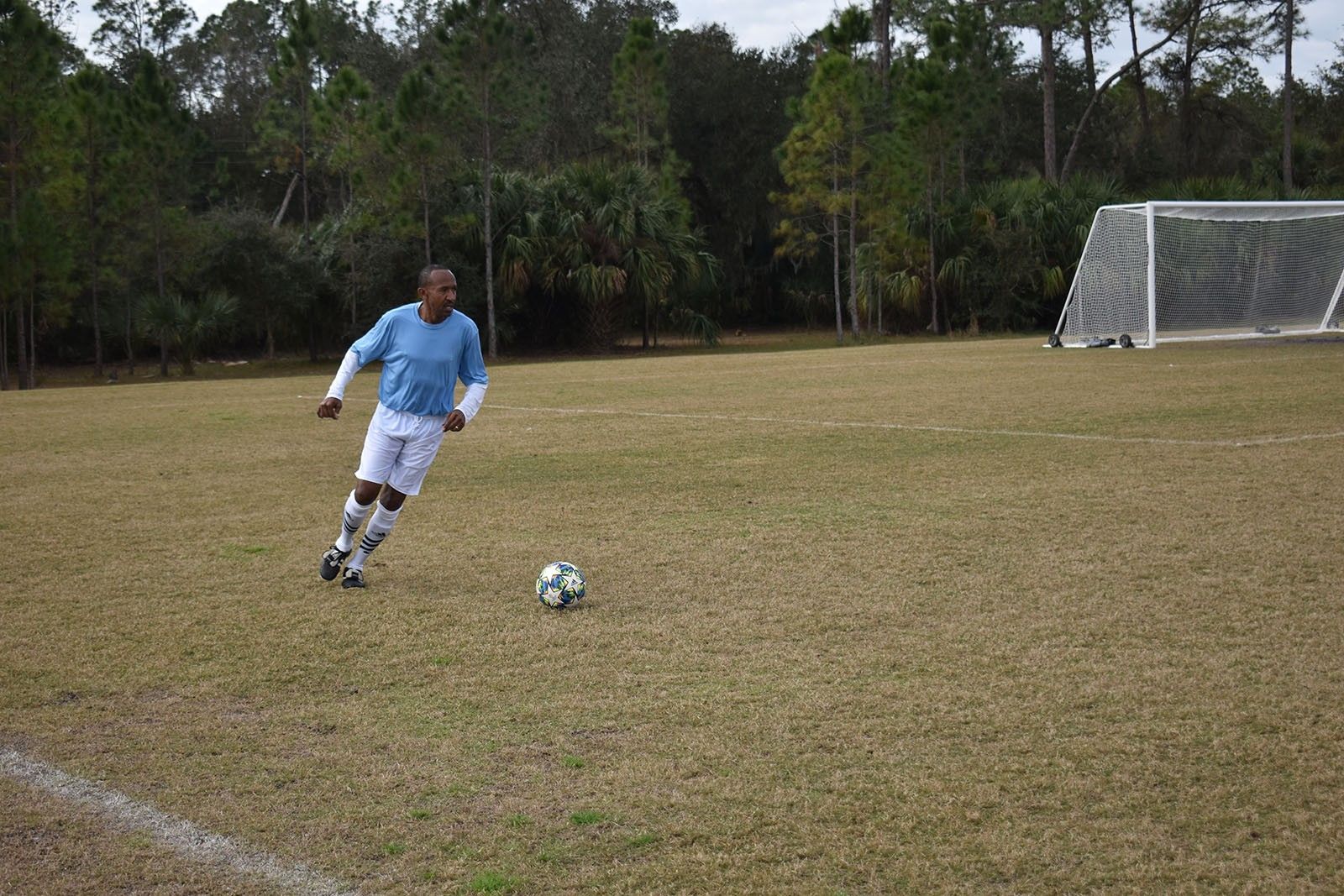 Soccer player in blue jersey dribbling a ball on a grassy field near a goal.