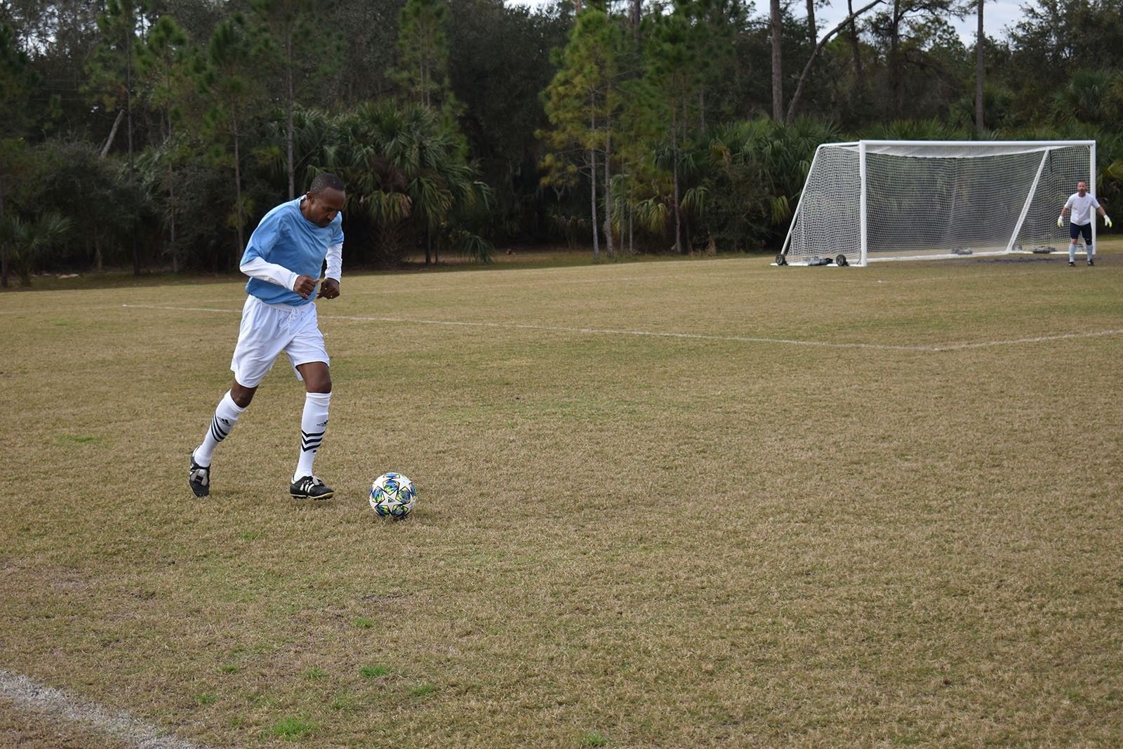 Soccer player in a blue jersey dribbling a ball on a field near a goal