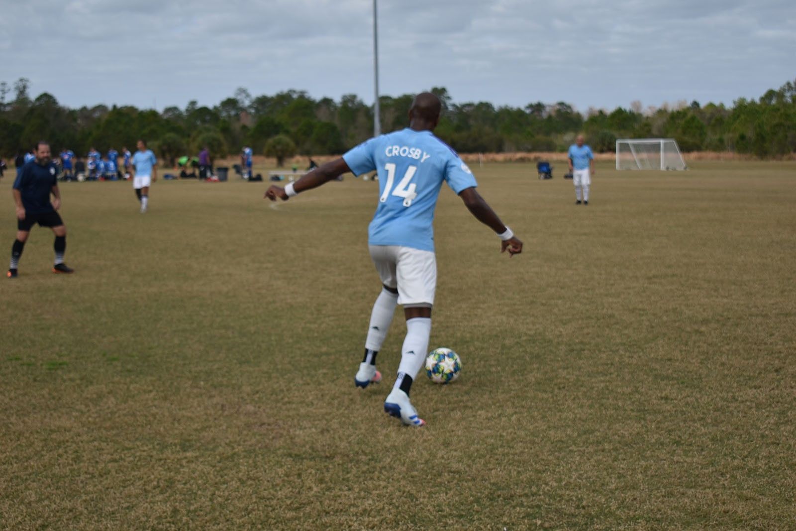 Soccer player in a light blue jersey dribbling on a grassy field during a match