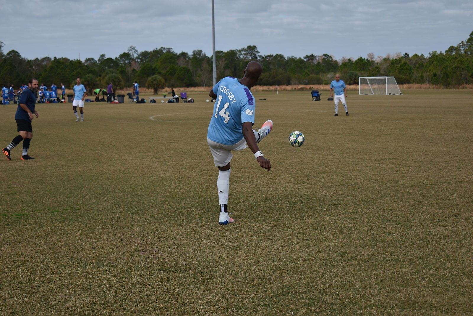 Soccer player in light blue jersey kicks a ball on a grassy field during a game