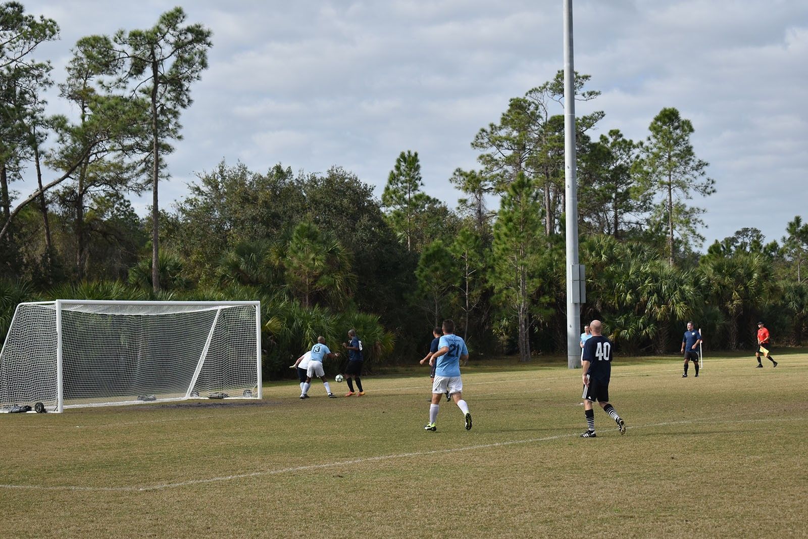 Soccer game near the goal on a grassy field, with players in blue and black uniforms.