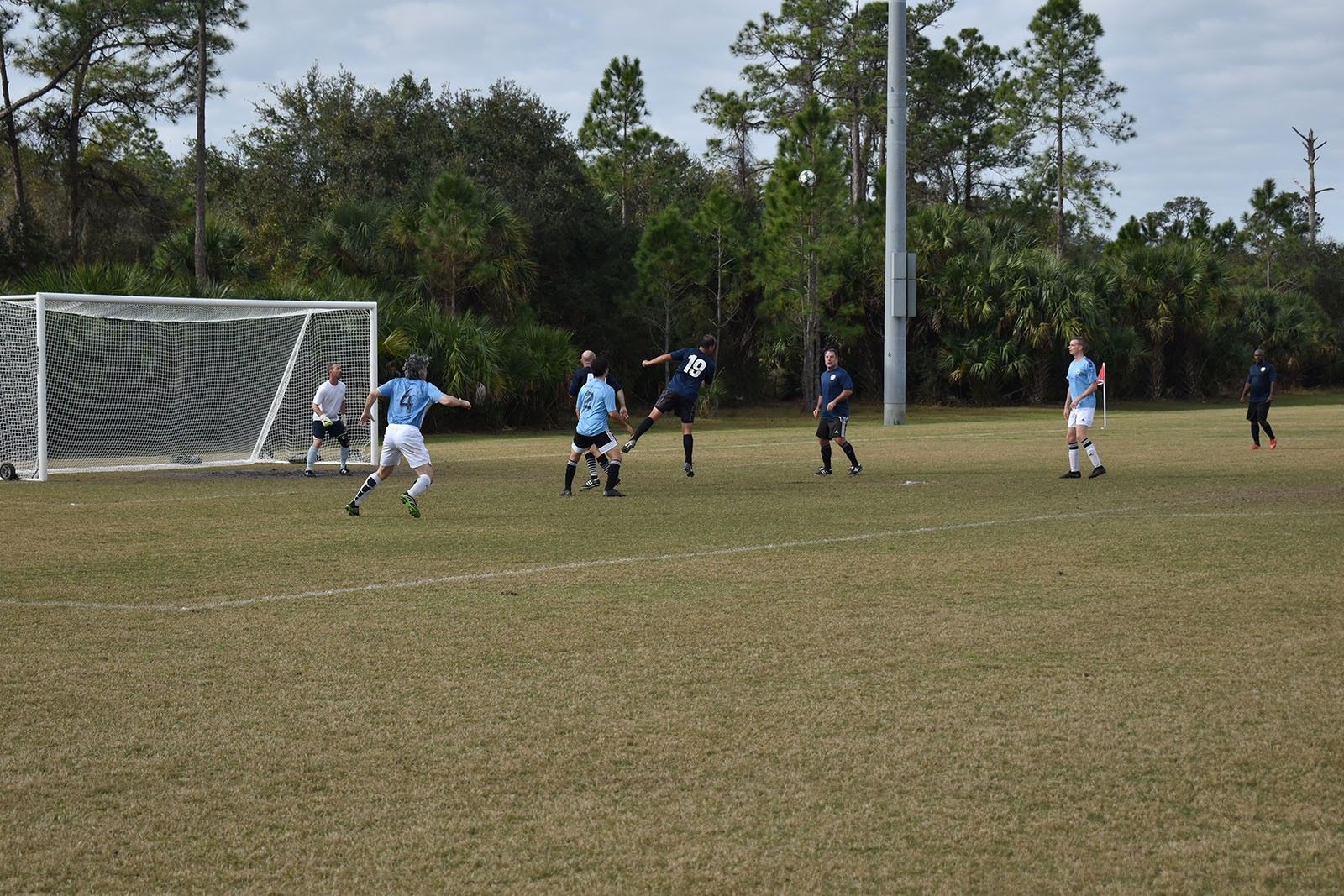 Soccer players in blue and white chase the ball near the goal on a grassy field.