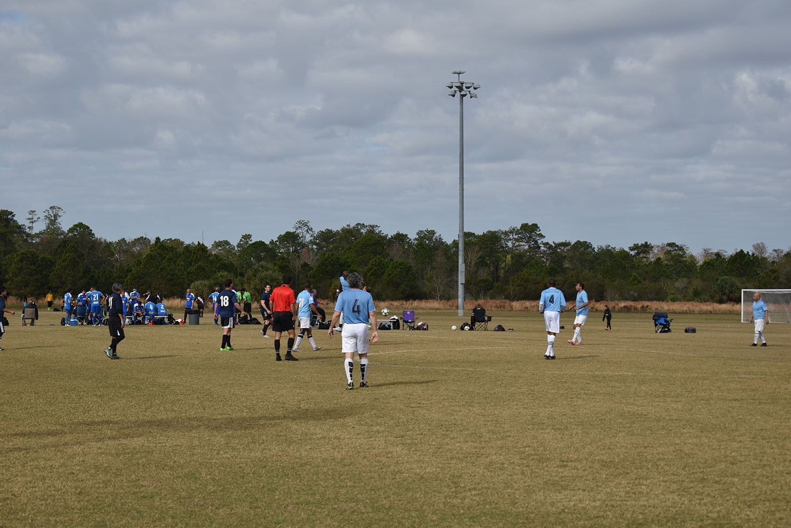 Soccer match on a grassy field with players in blue, white, and orange under a cloudy sky