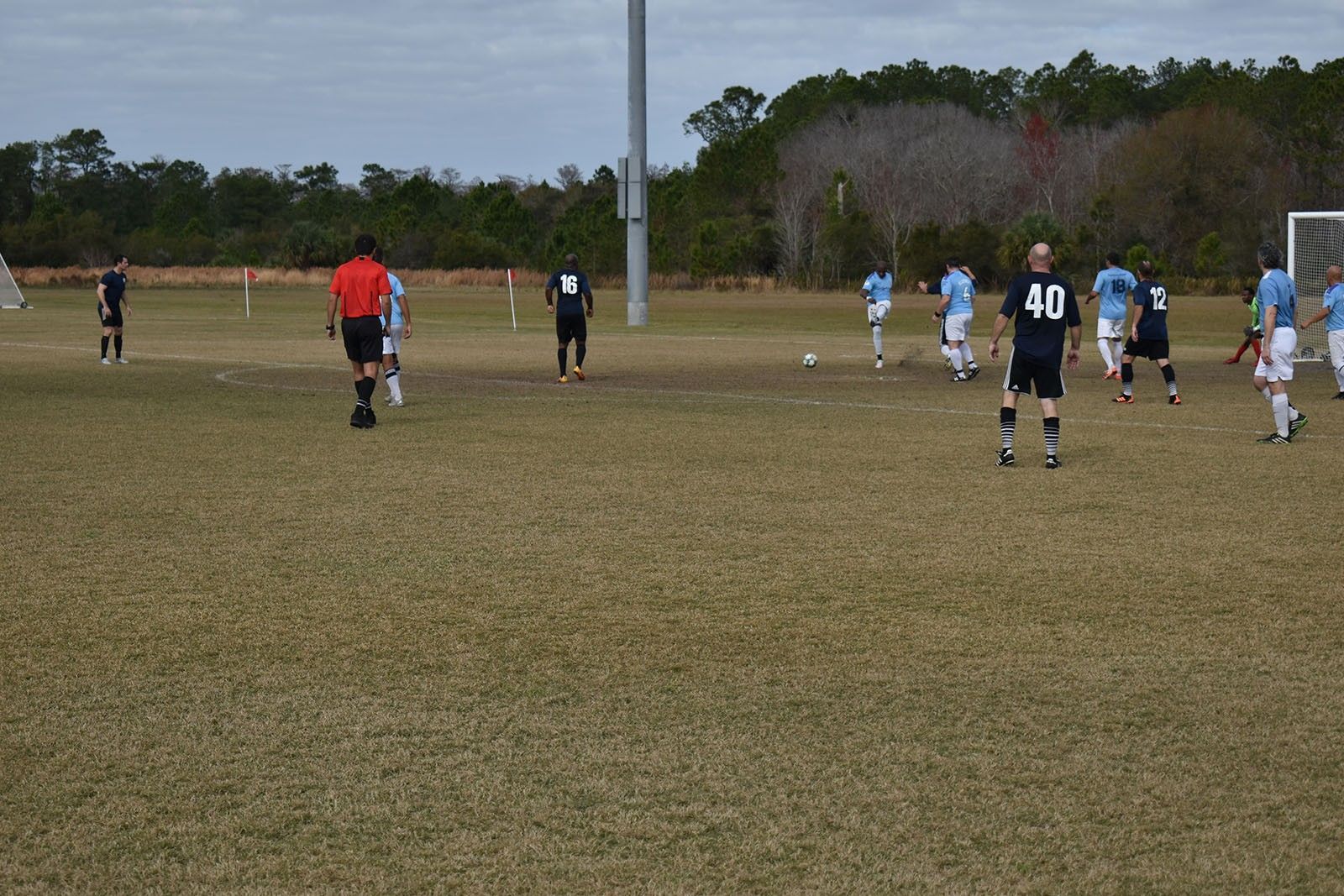 Soccer game on a grassy field with players in black, white, and blue uniforms near the goal