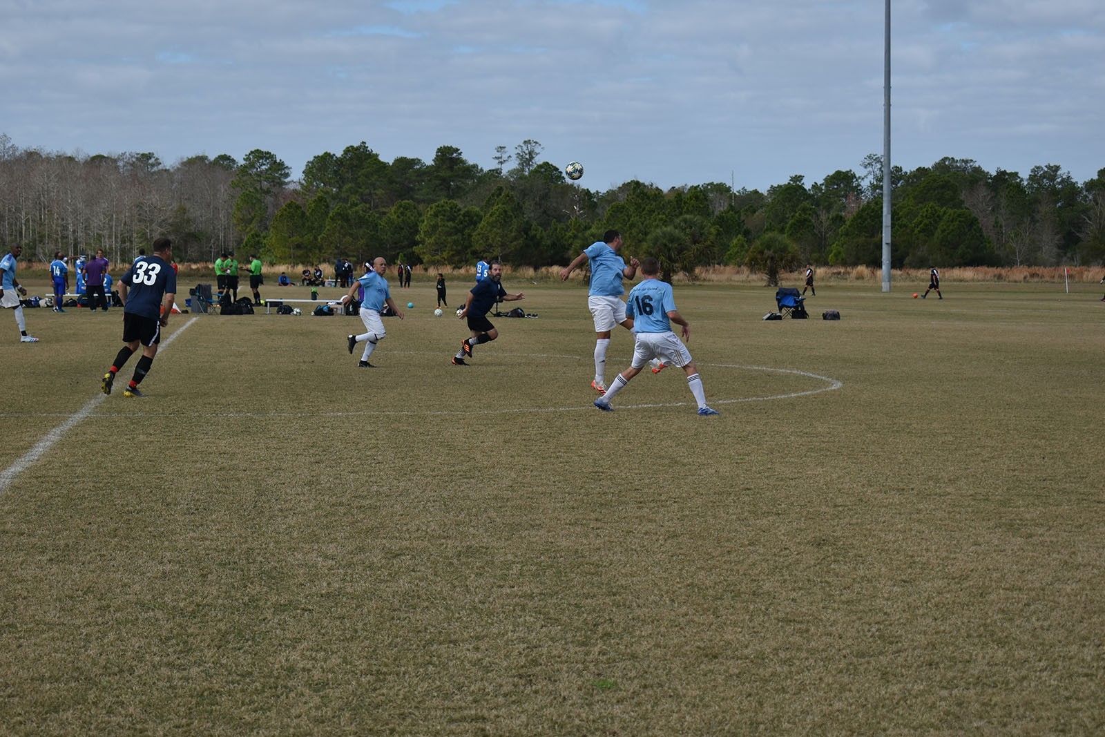 Soccer players in blue uniforms sprint across a grassy field during a match.