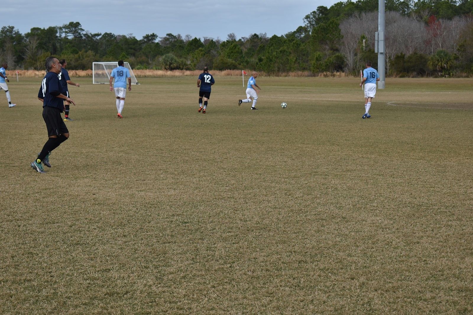 Youth soccer players on a grassy field, with one player in black running toward the ball.
