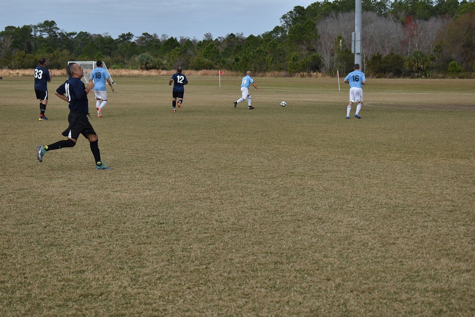 Soccer players in dark and light uniforms running on a grassy field under a cloudy sky