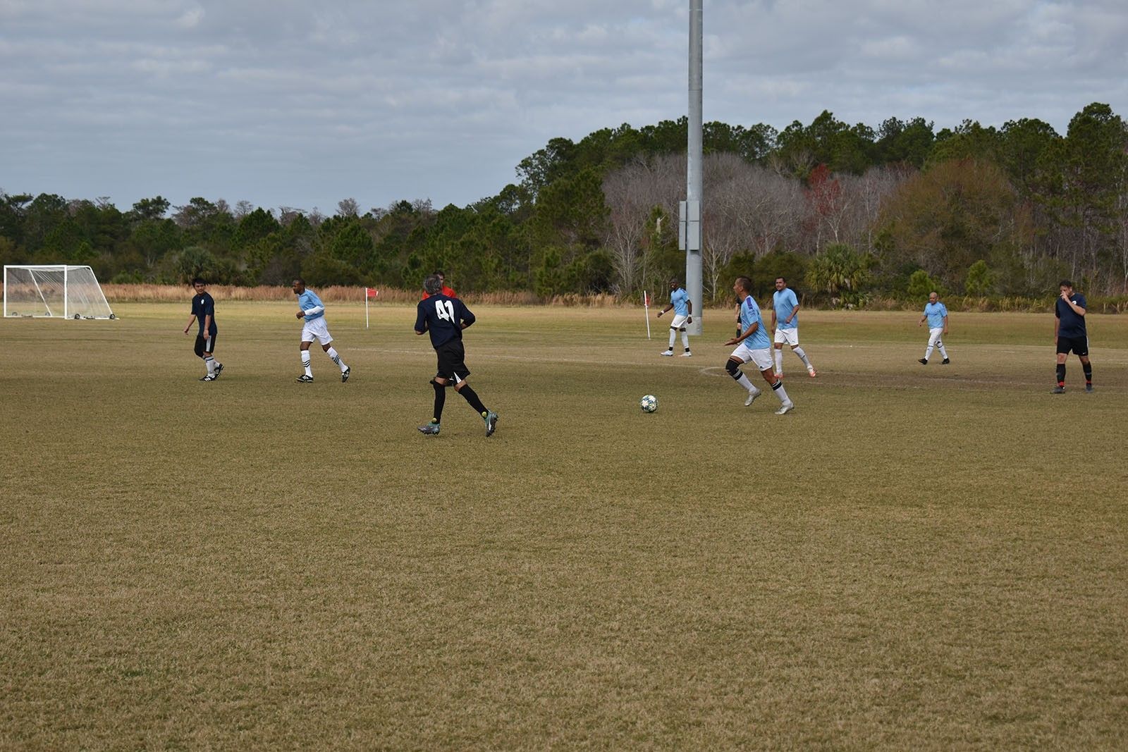 Soccer game on a grassy field with players in light blue and black uniforms near the goal