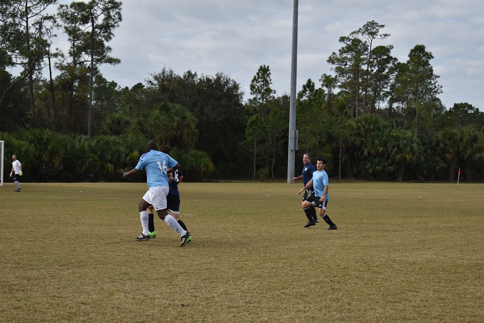 Soccer players in blue uniforms running on a grassy field with trees in the background