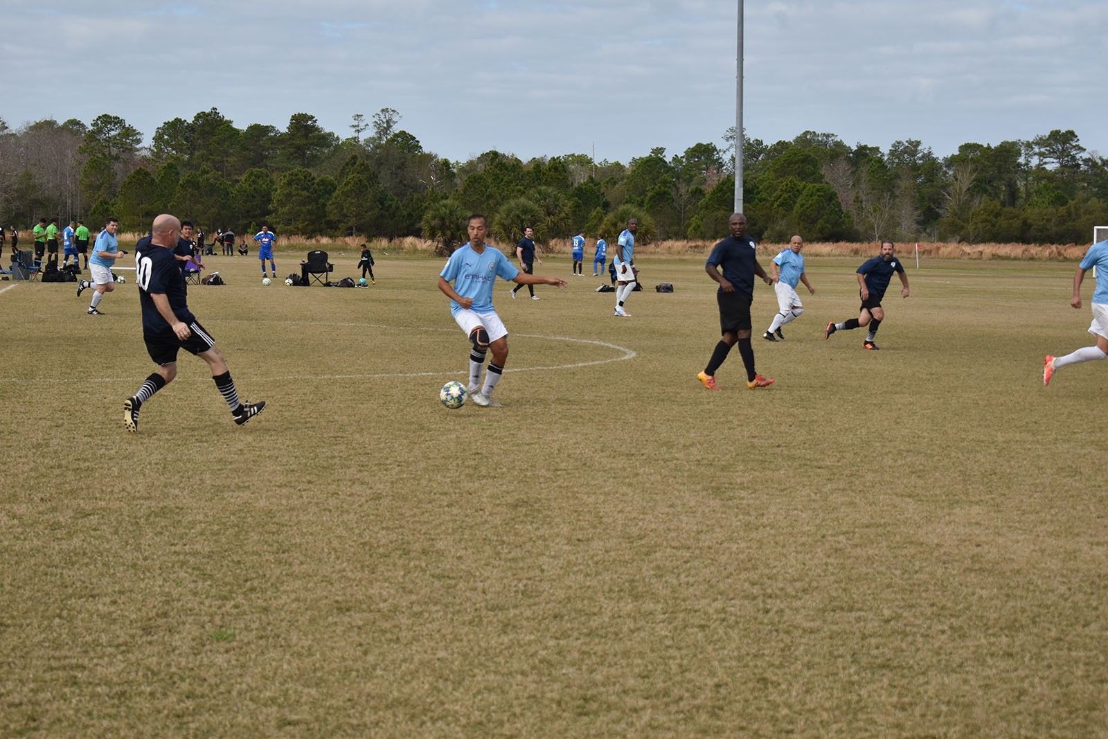Soccer players in blue and black uniforms play on a grassy field under a cloudy sky.