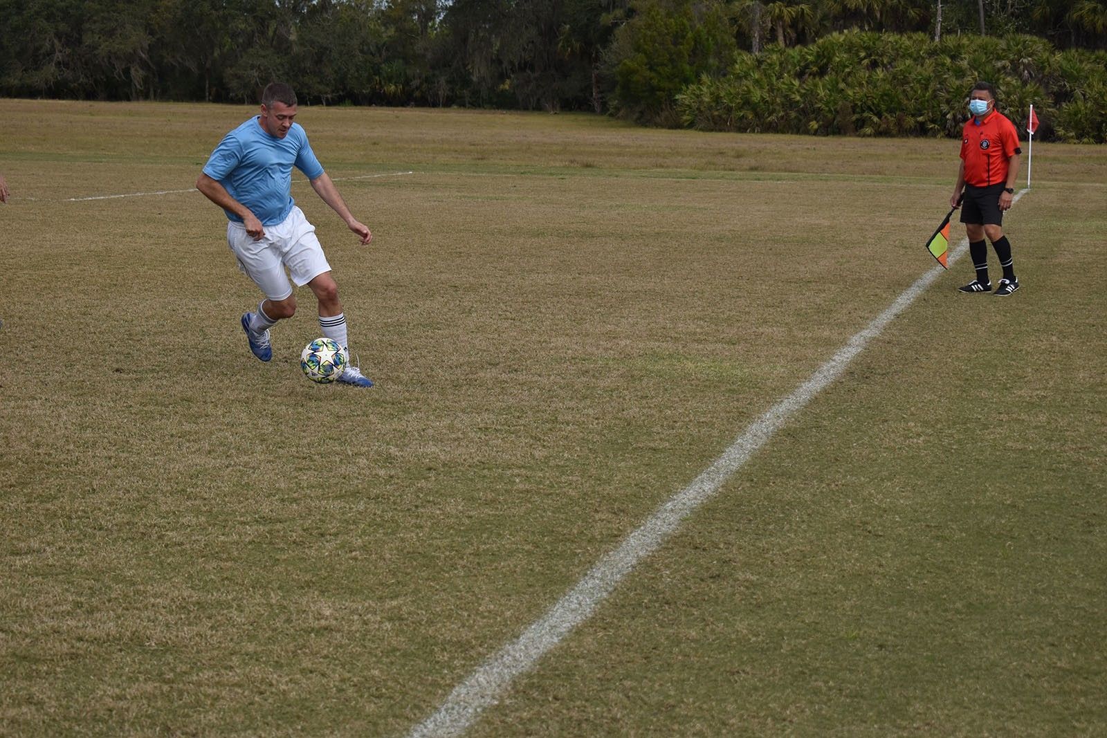 Soccer player in blue dribbles ball on a field toward a referee in orange