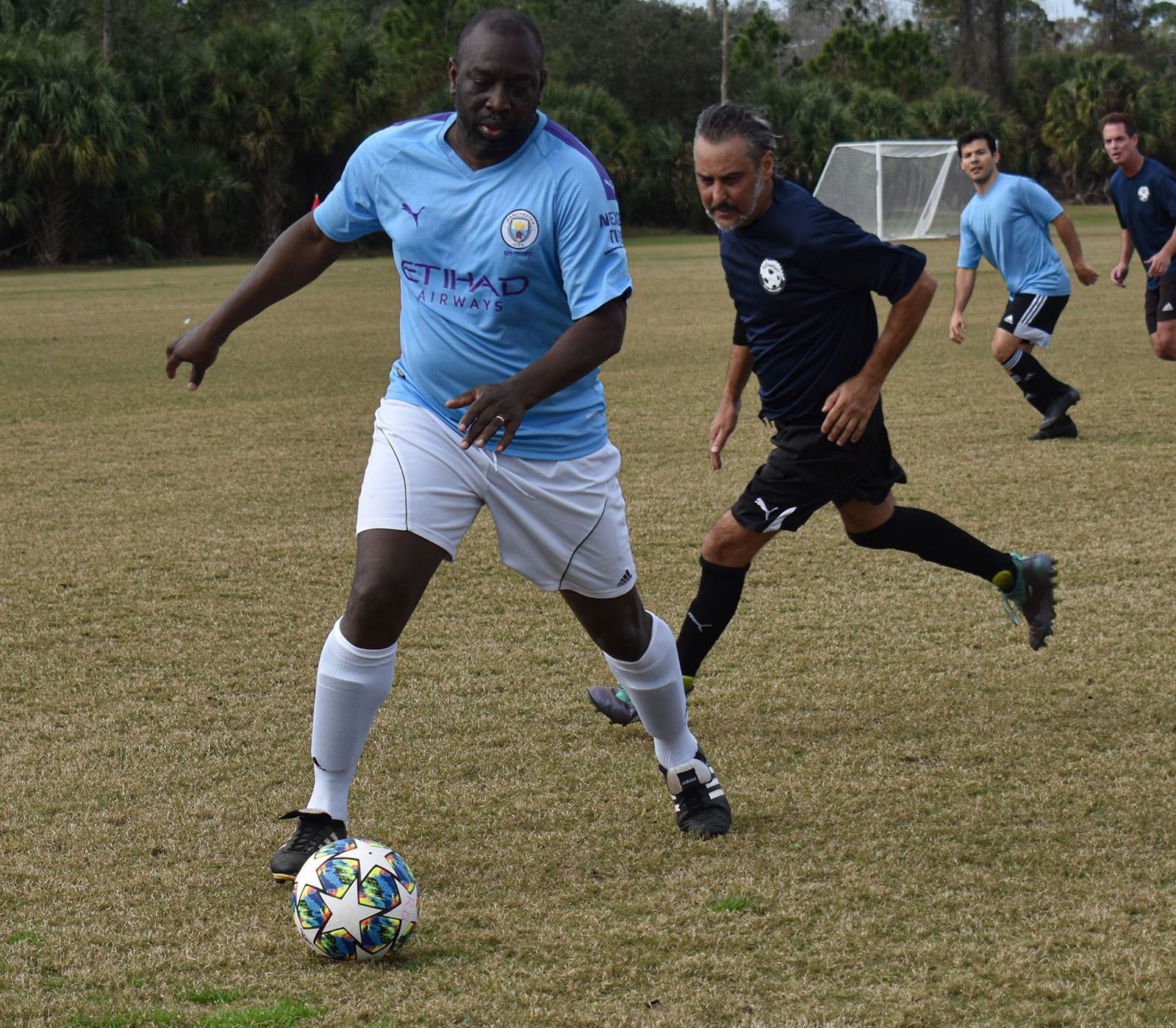 Soccer players battling for the ball on a grassy field, with a light blue jersey in the foreground