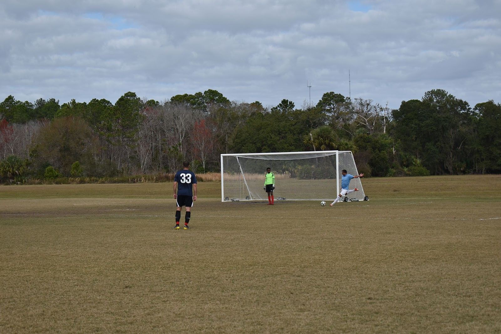 Soccer goal on a grassy field with a goalkeeper and a player standing nearby