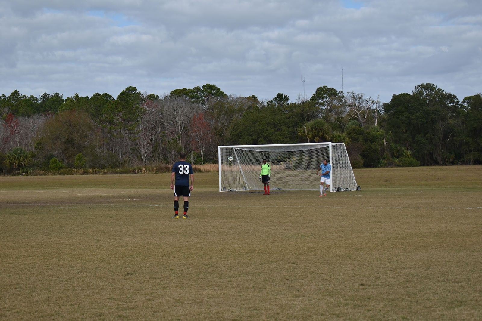 Soccer field with a player near the goal and a goalkeeper in front of the net.