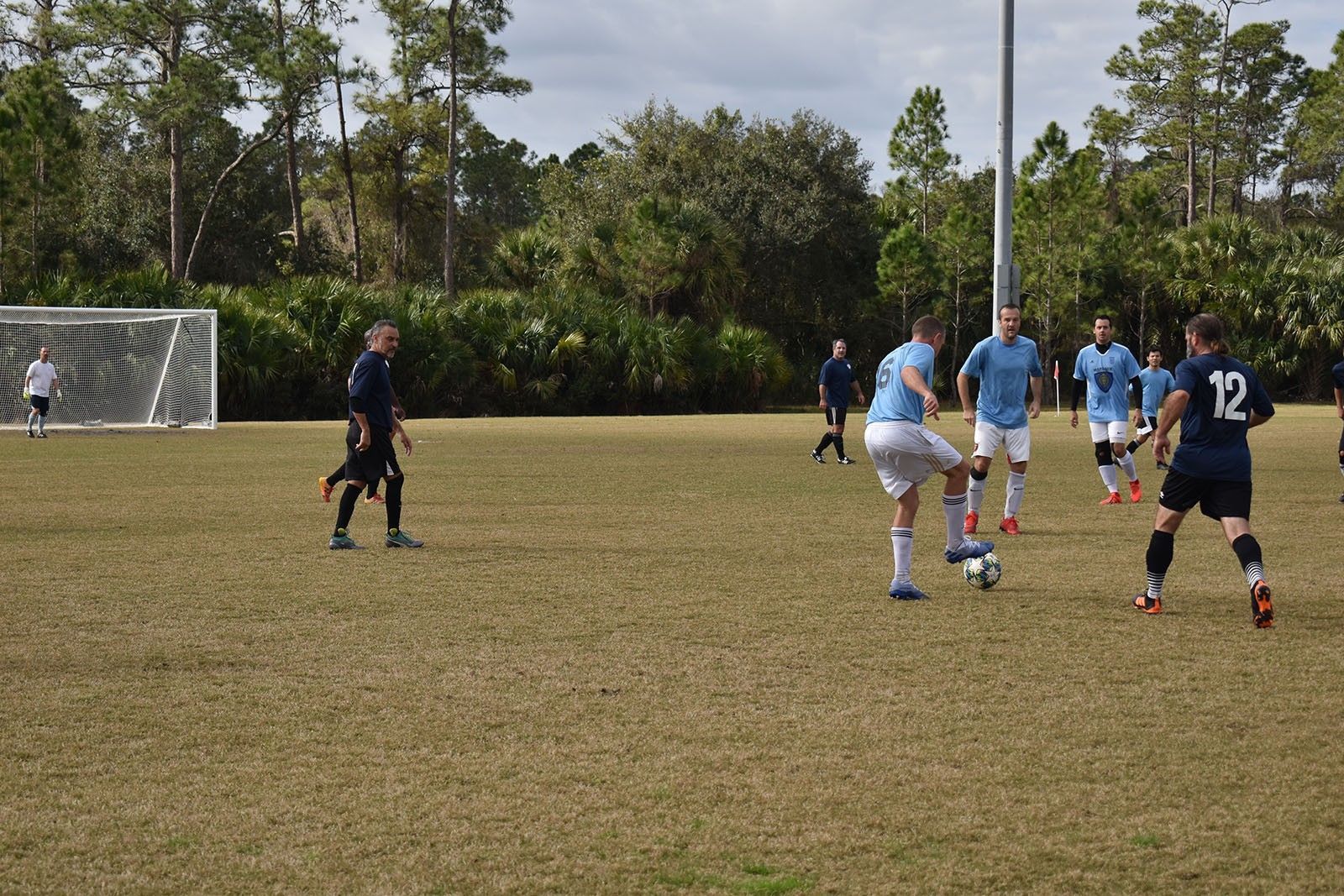 Soccer players in blue and navy compete near the goal on a grassy field.