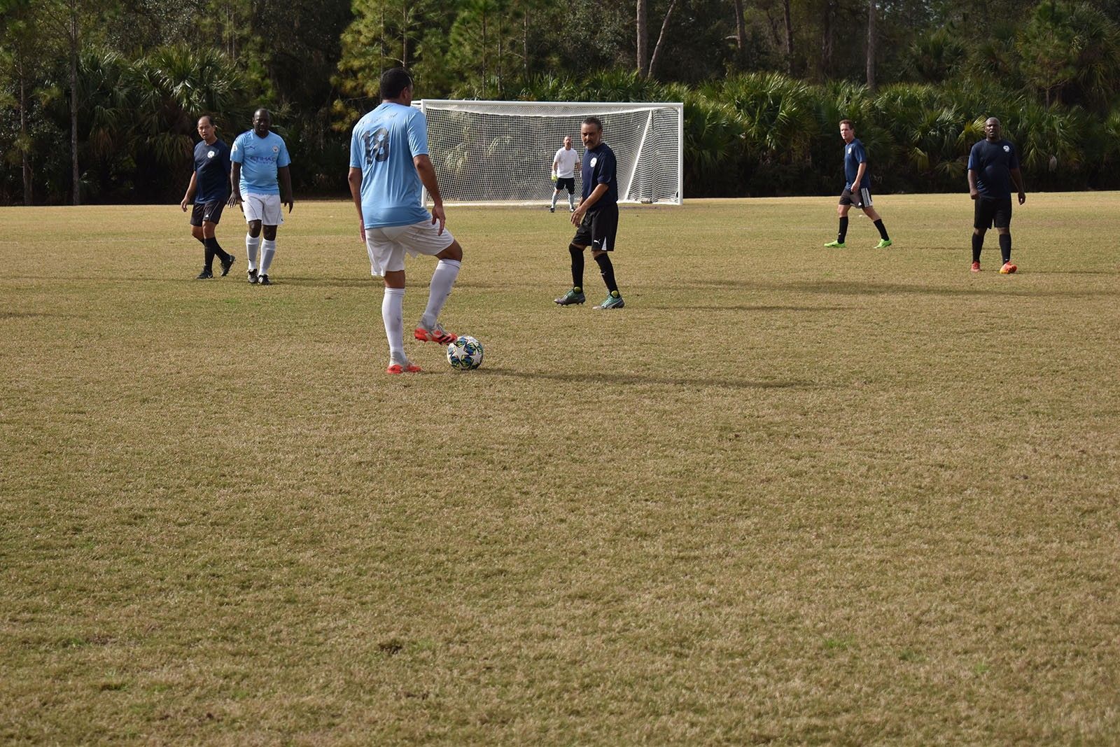 Soccer players on a grassy field during a match, with a goal in the background