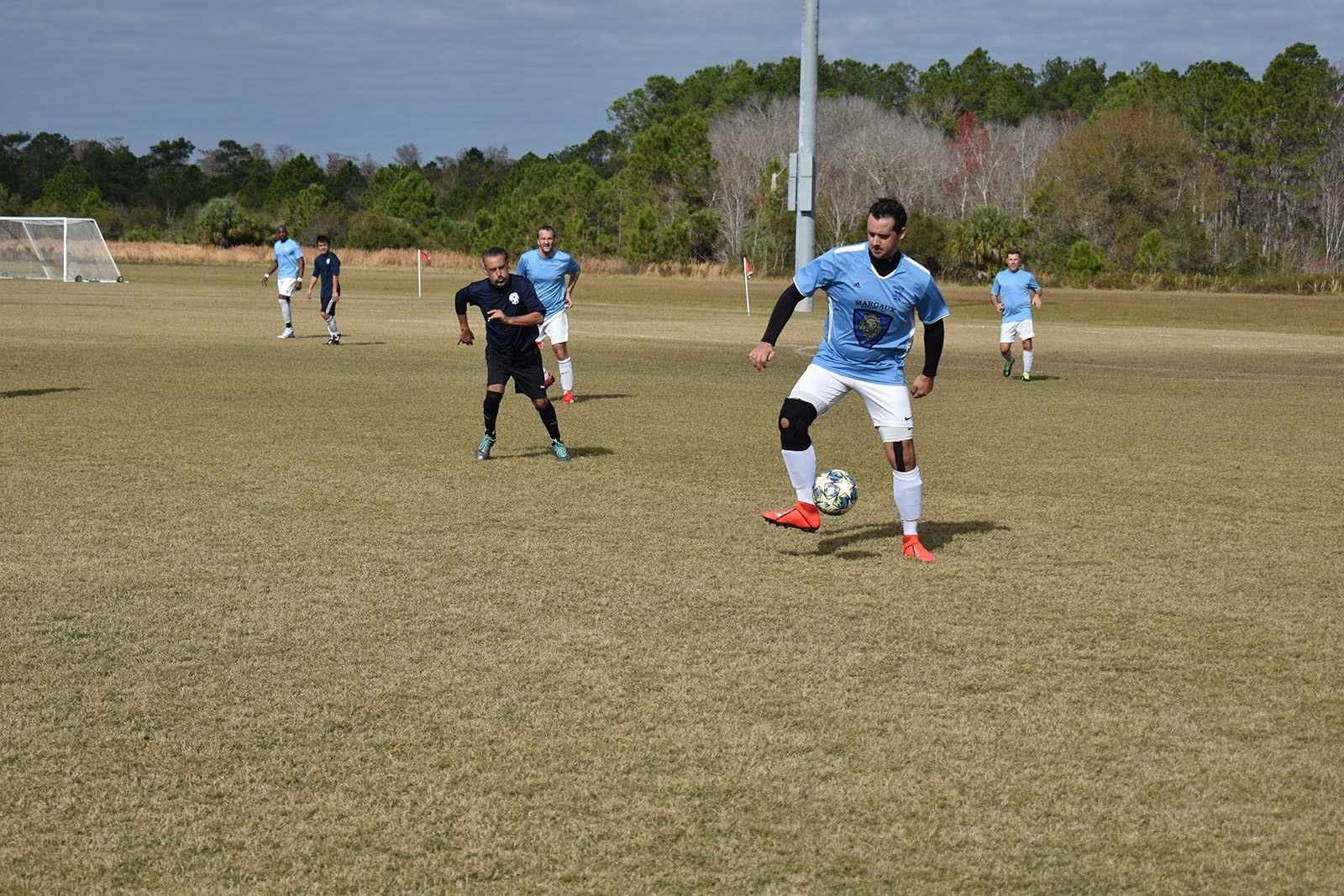 Soccer players in blue and black uniforms on a grassy field, with one player dribbling near the foreground.