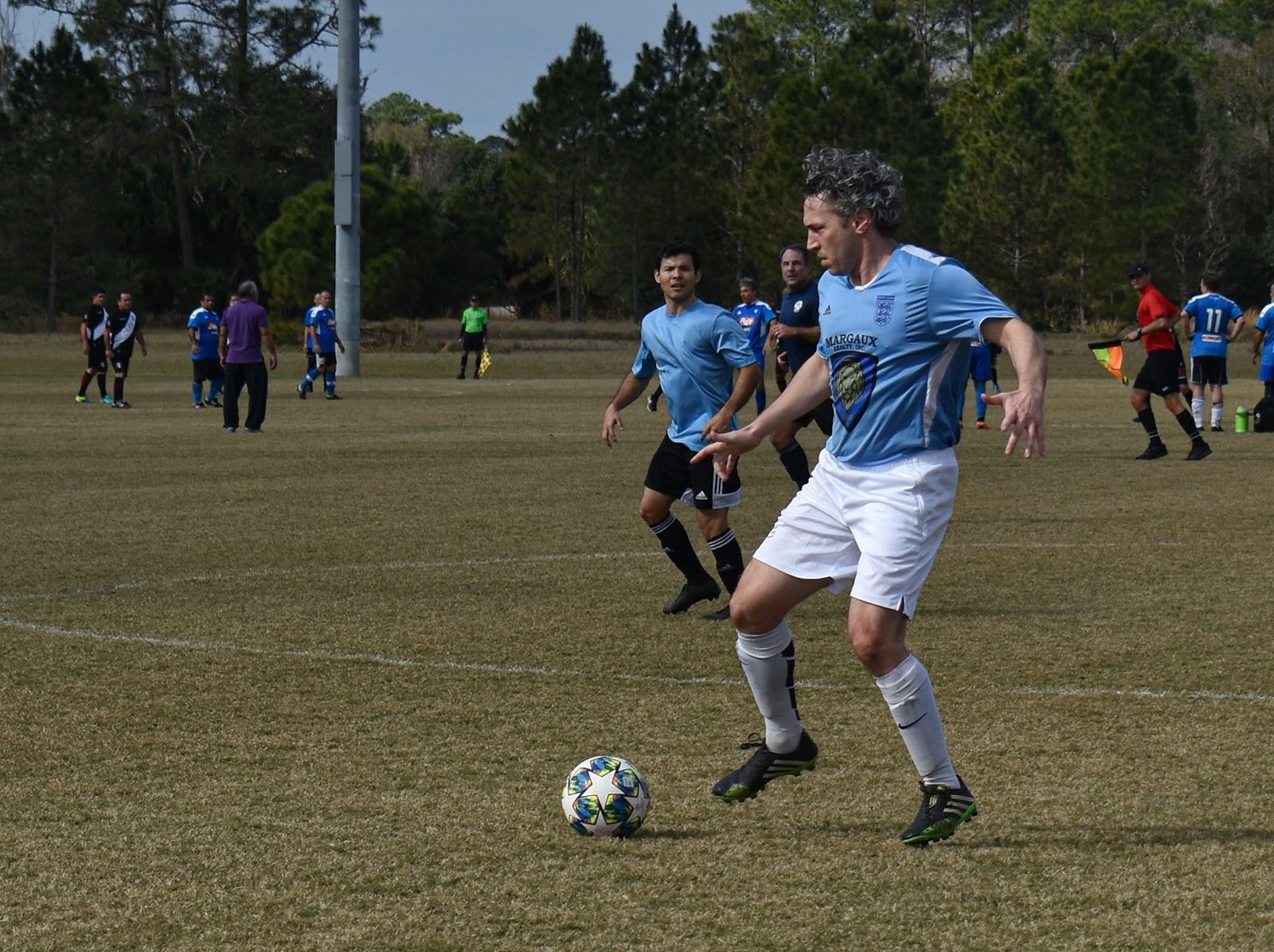 Soccer players in blue jerseys on a grassy field, with one dribbling the ball in the foreground.