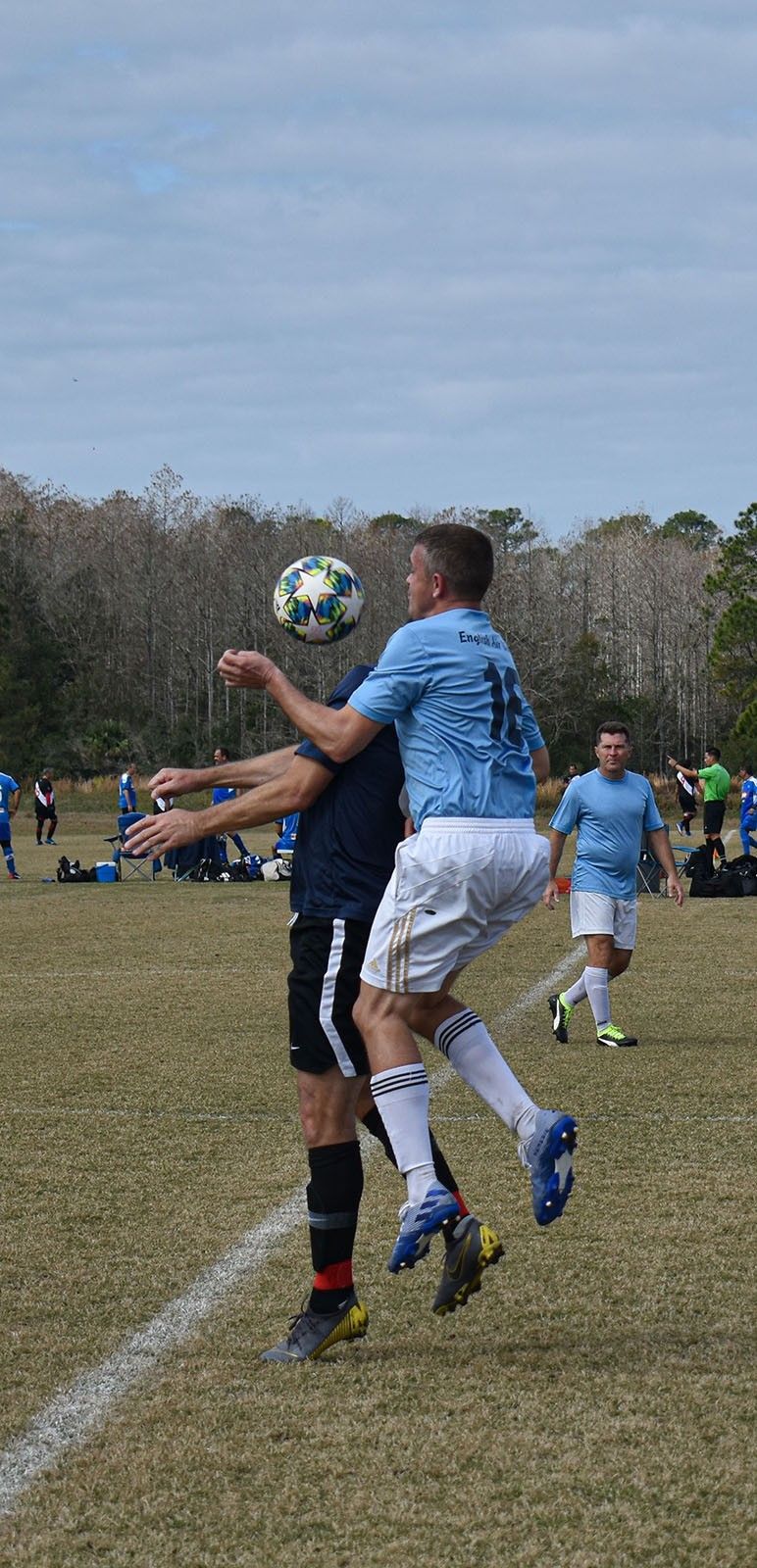 Two soccer players jump to head a ball on a grassy field during a match.