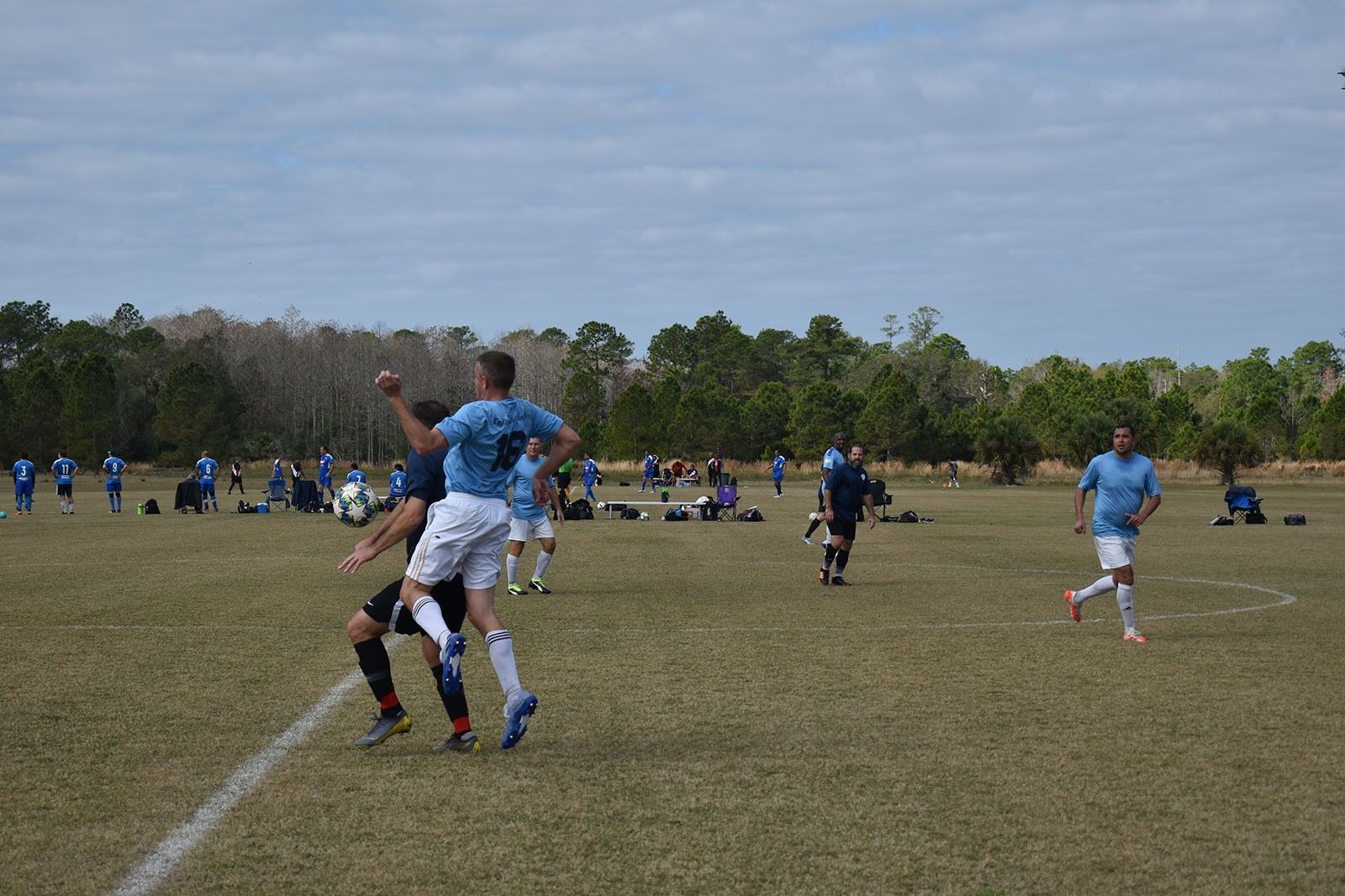 Soccer players in blue uniforms compete on a grassy field under a cloudy sky.