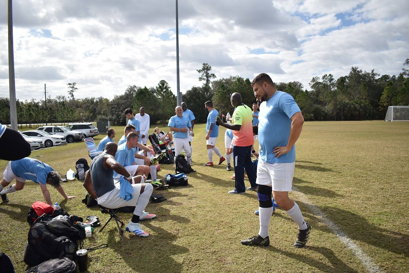 Soccer team gathered on a grassy field during a break, with players in blue jerseys and one standing in the foreground.