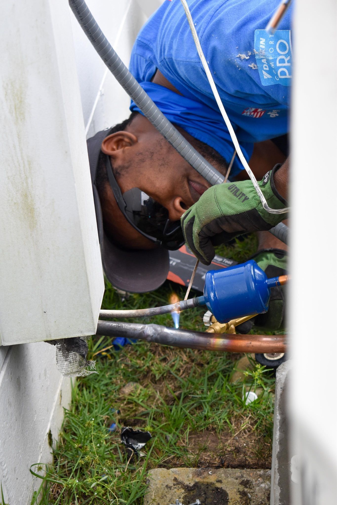 Technician in blue shirt working on outdoor copper pipes beside a building.