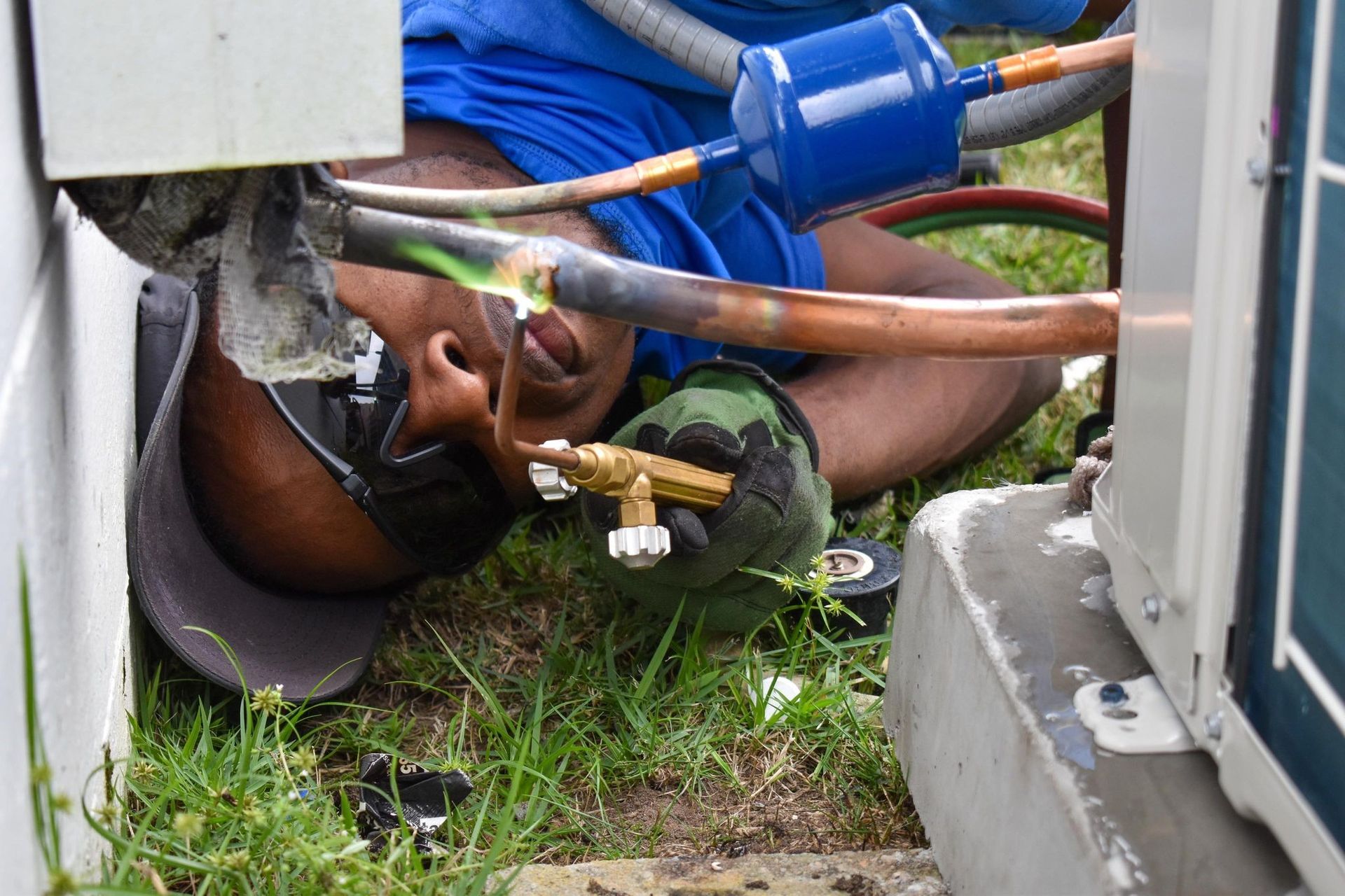 Person trapped under blue utility equipment in a grassy area, with hoses and cables nearby.