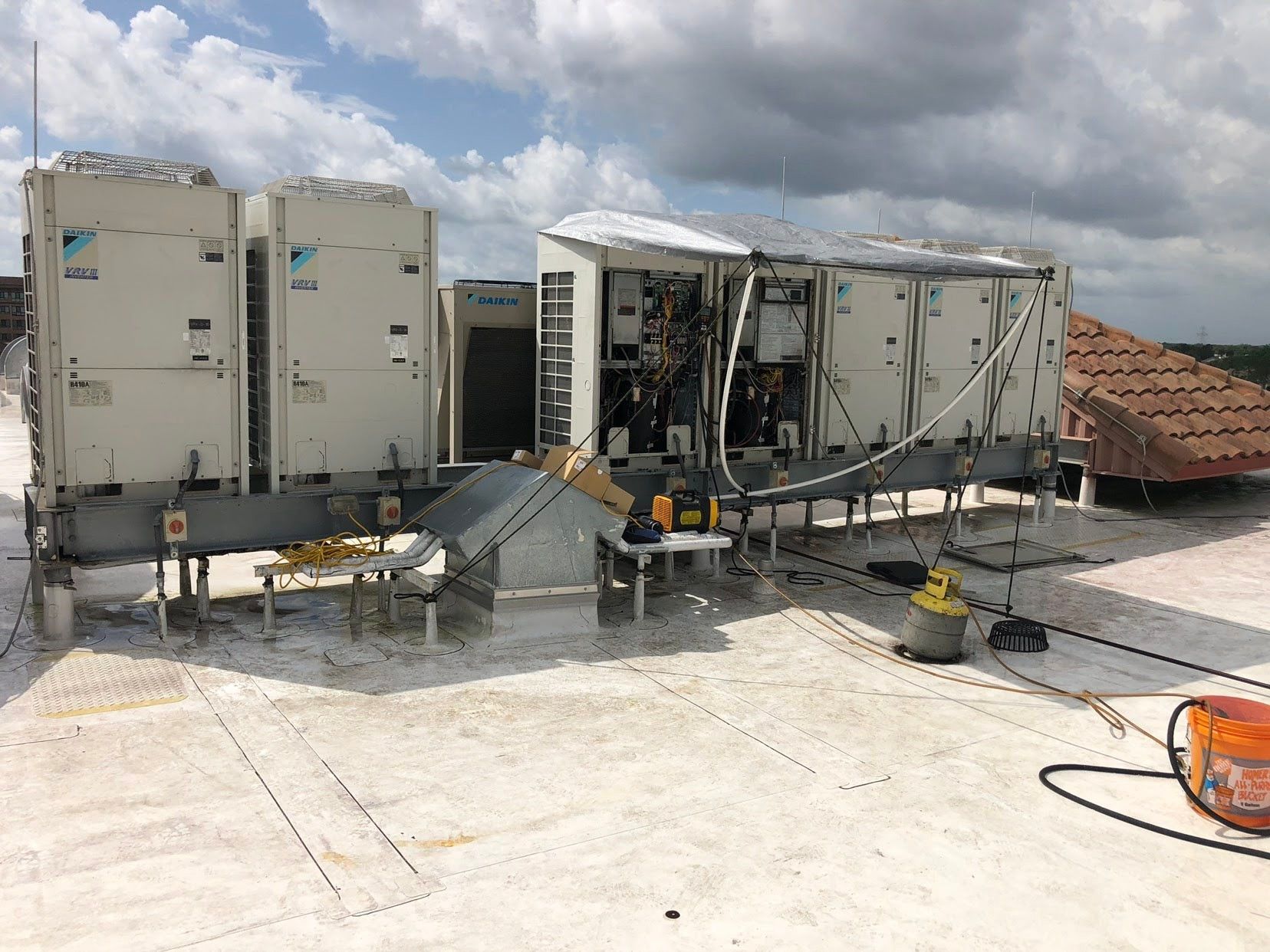 Damaged rooftop HVAC unit with bent metal panels and debris on a concrete roof under cloudy skies