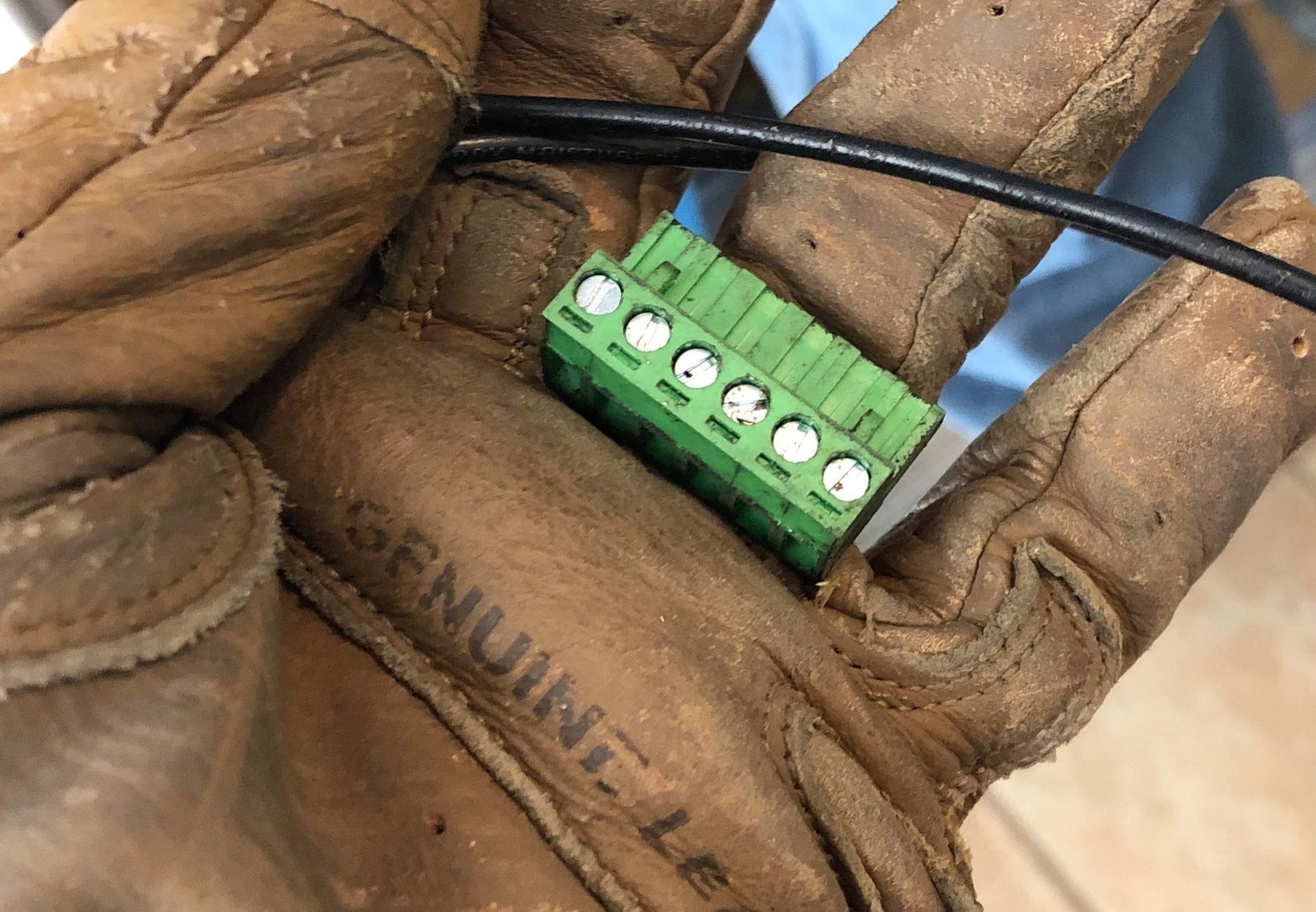 Gloved hand holding a small green terminal block with a black wire attached