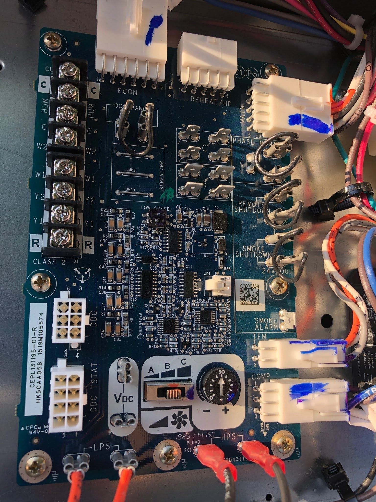 Close-up of a blue circuit board with white connectors, wiring, and red jumper leads on a workbench.