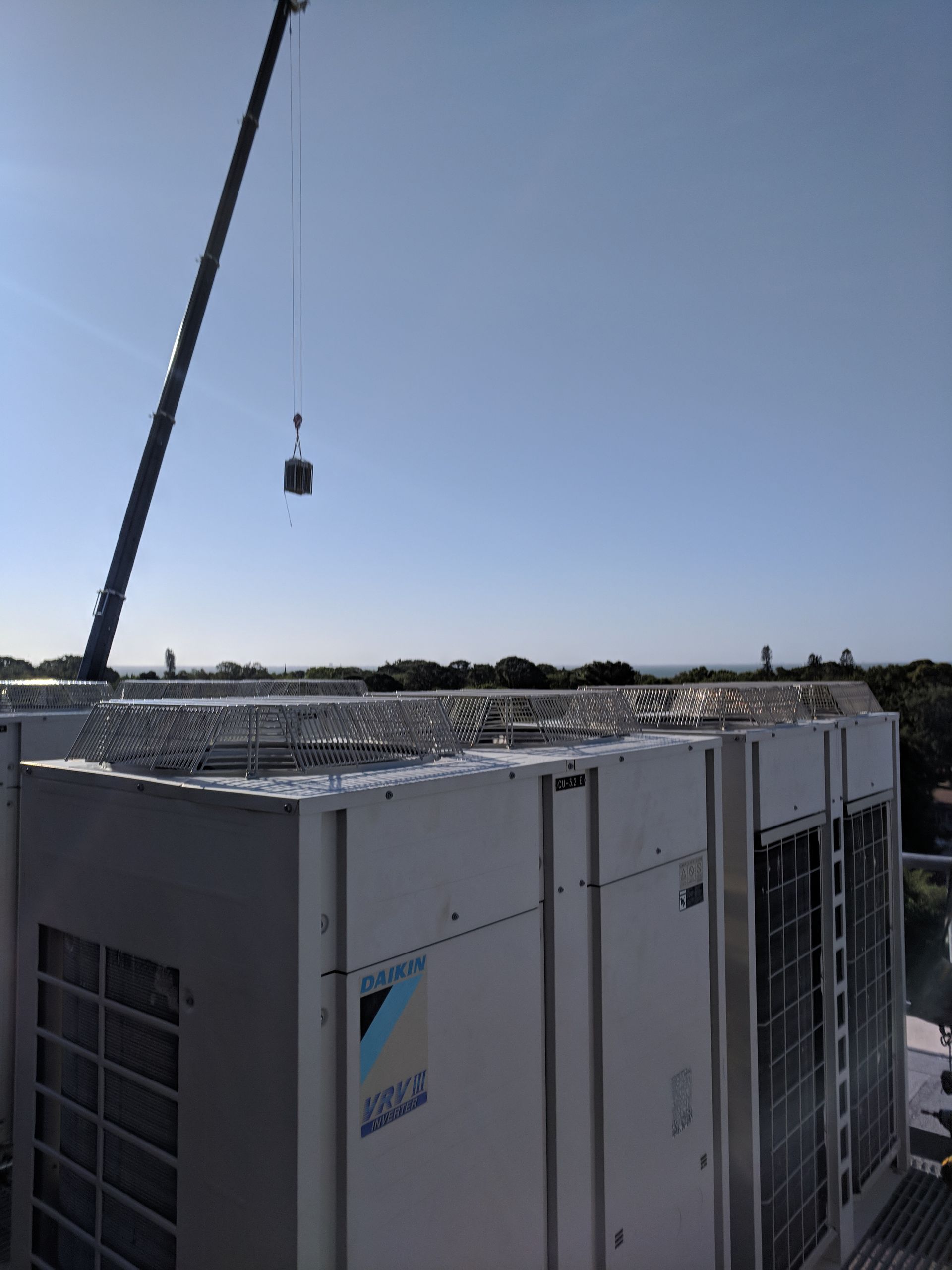 Large rooftop HVAC units with a crane lifting equipment above them under a clear blue sky.