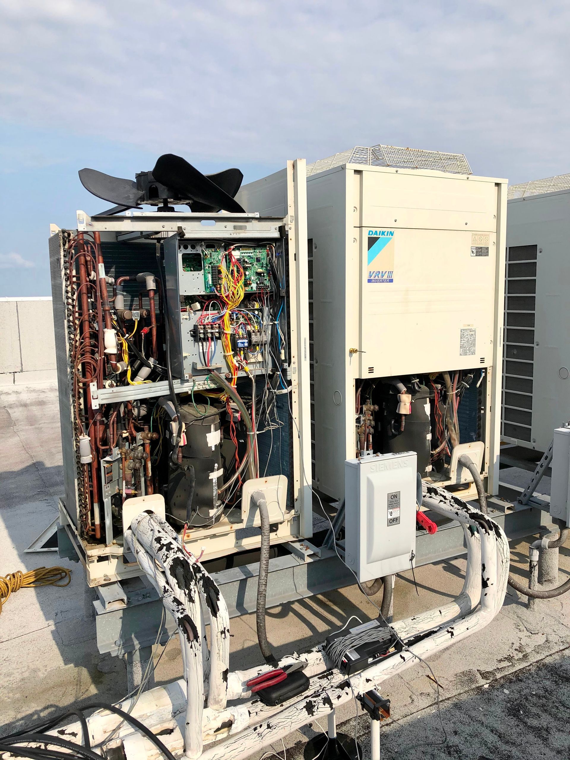 Damaged rooftop HVAC units with exposed wiring and panels on a flat roof