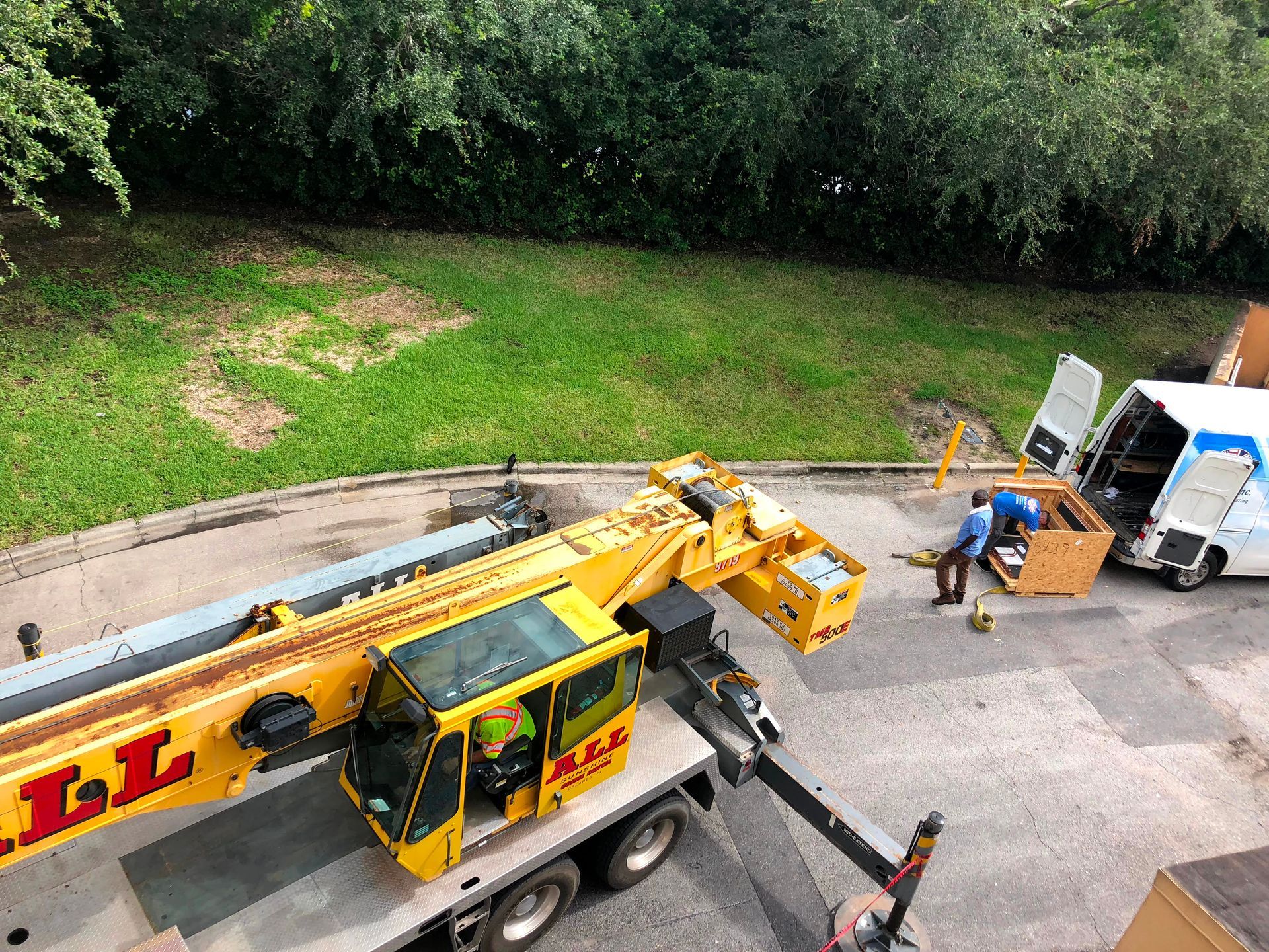 Yellow utility truck with extended crane arm parked beside a road, with workers and equipment nearby