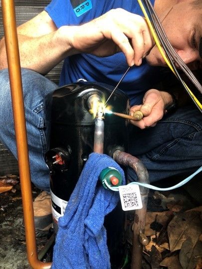 Person welding a black metal pipe outdoors, with sparks and a blue cloth draped over it.